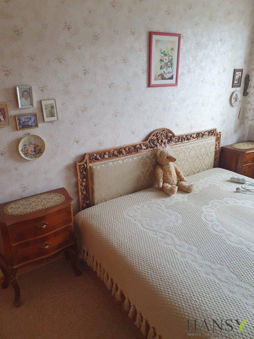 Schlafzimmer mit kunstvoll geschnitztem Holzbettrahmen, gemusterter Tapete und traditionellen Möbeln.