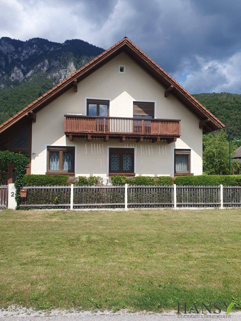 Vorderansicht des Hauses mit Balkon und Satteldach, eingebettet in eine malerische Berglandschaft.