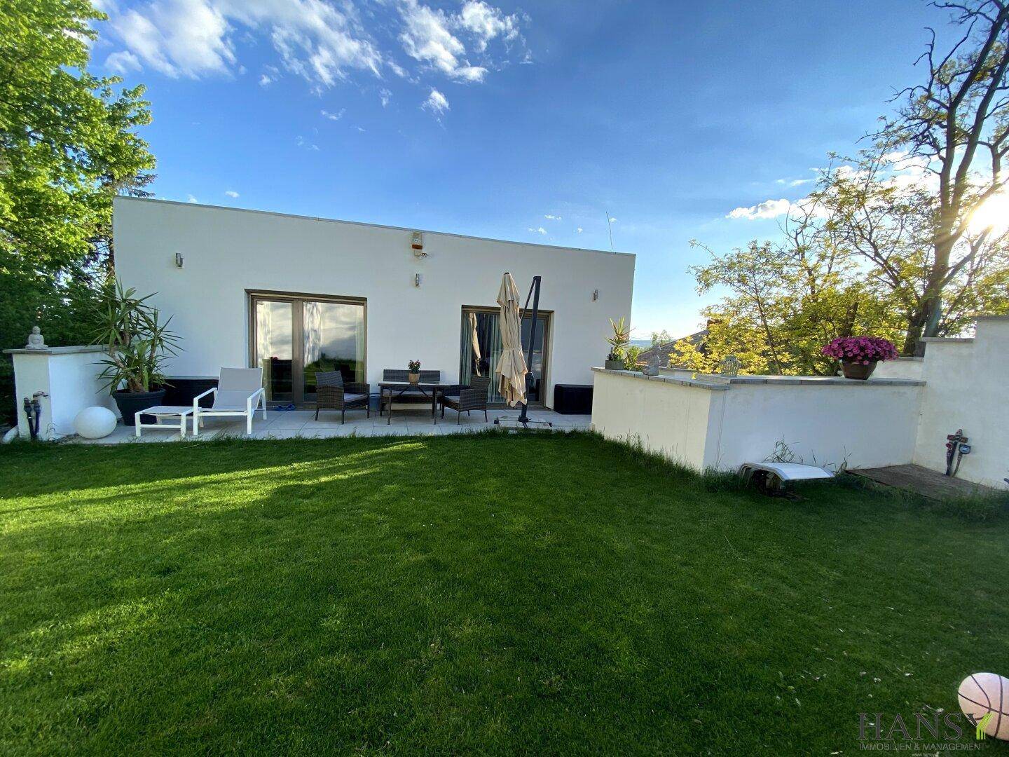 Moderne Hausrückseite mit gepflegtem Rasen und einer möblierten Terrasse unter blauem Himmel.