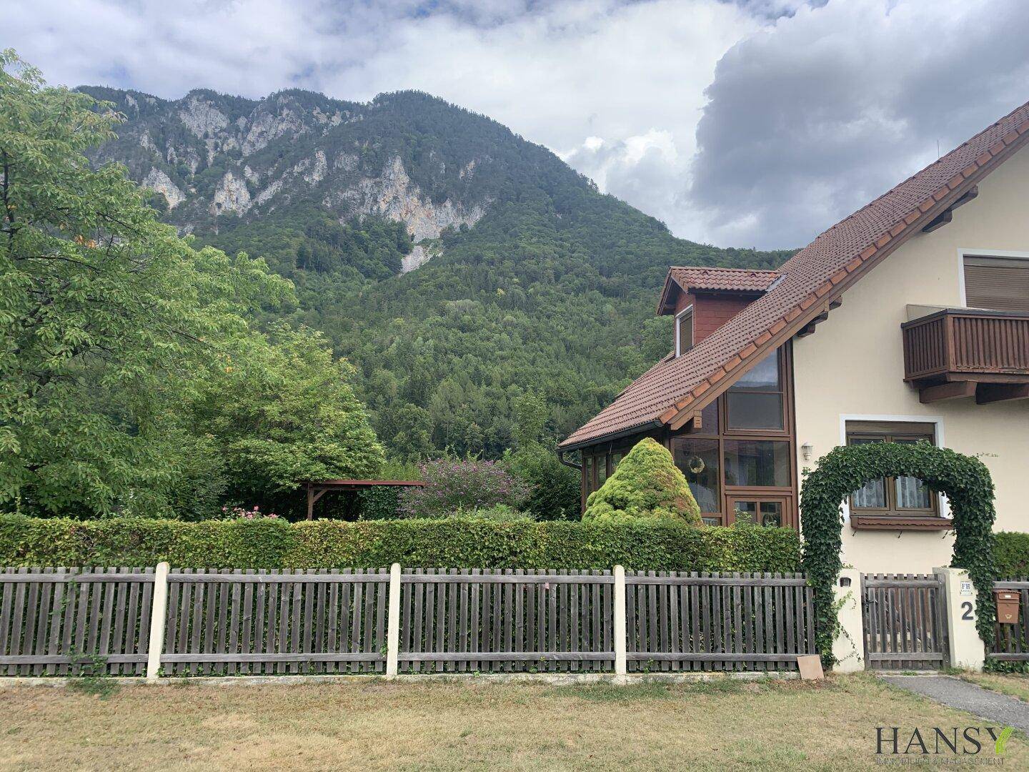 Seitenansicht des Hauses mit Wintergarten und Blick auf die bewaldeten Berge und Hecken.