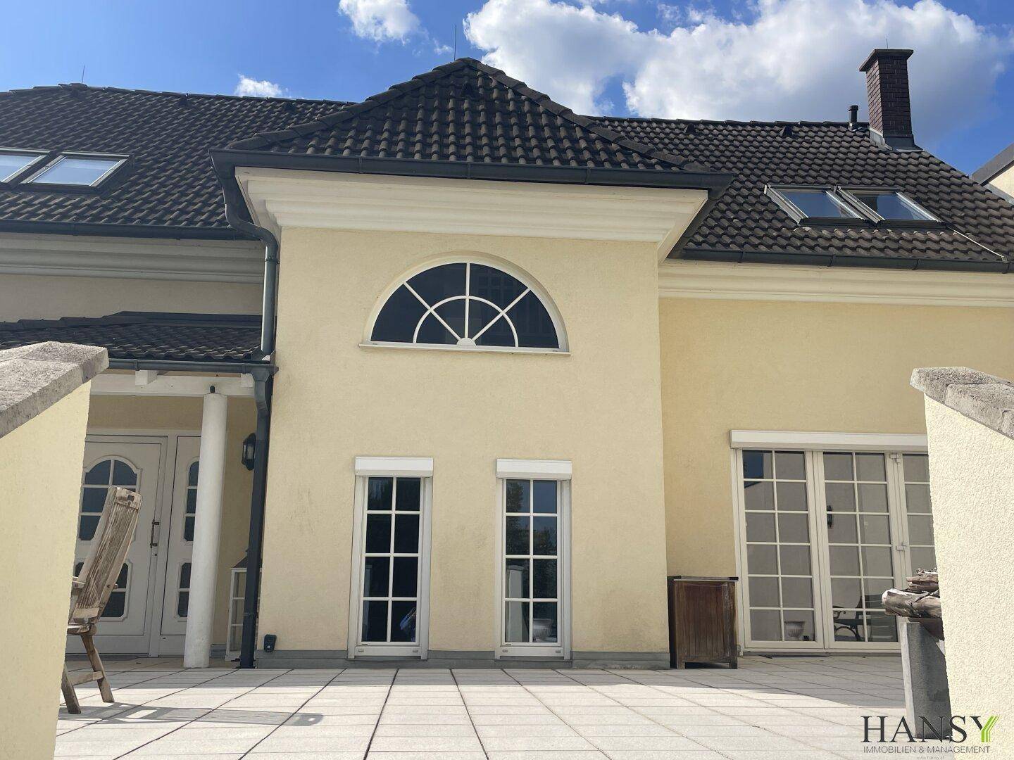 Detailansicht der Hausfassade mit großer Rundbogenfenster und Zugang zur Terrasse.