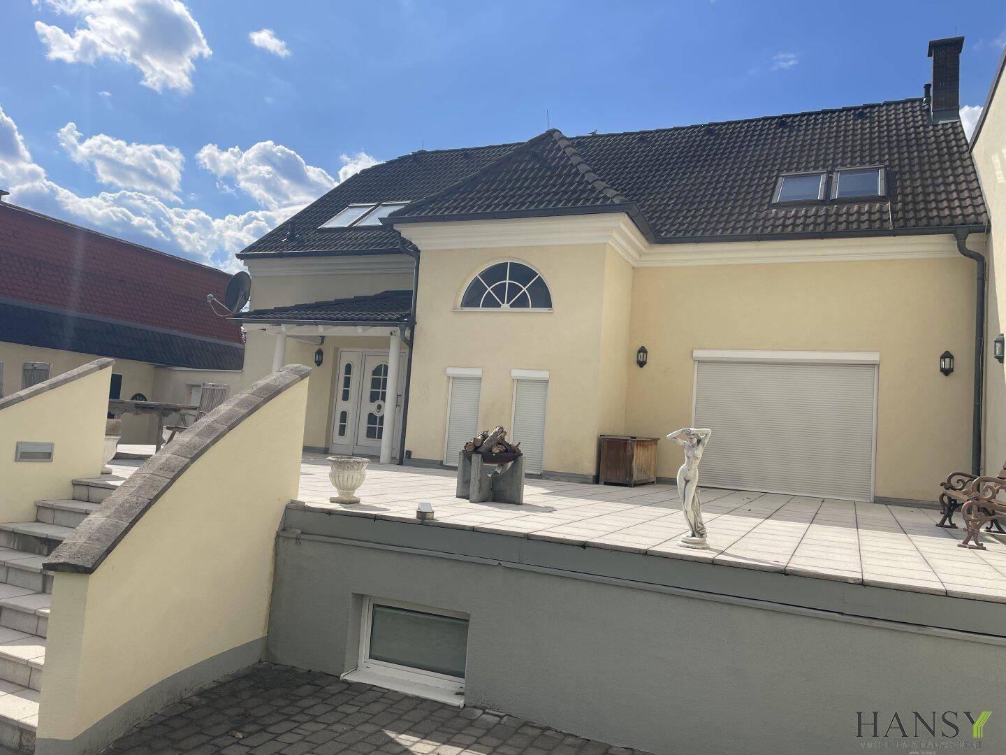 Seitenansicht des Hauses mit großer Terrasse, Garage im Untergeschoss und Gartenblick.