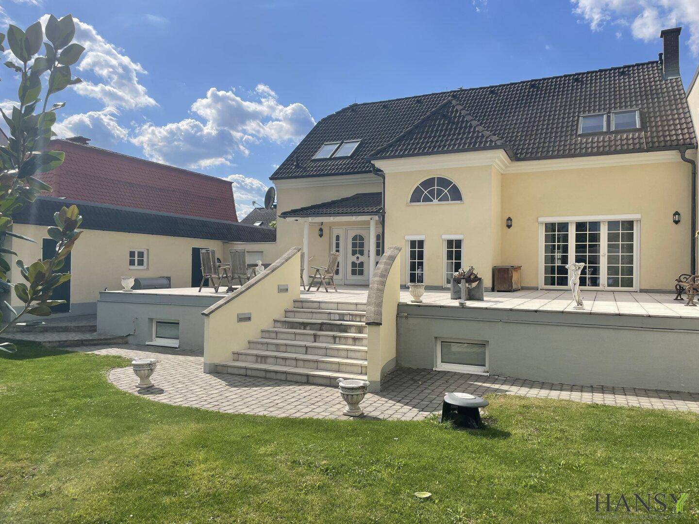 Ansicht des Hauses vom Garten aus mit großer Terrasse, Außentreppe und Nebengebäude.