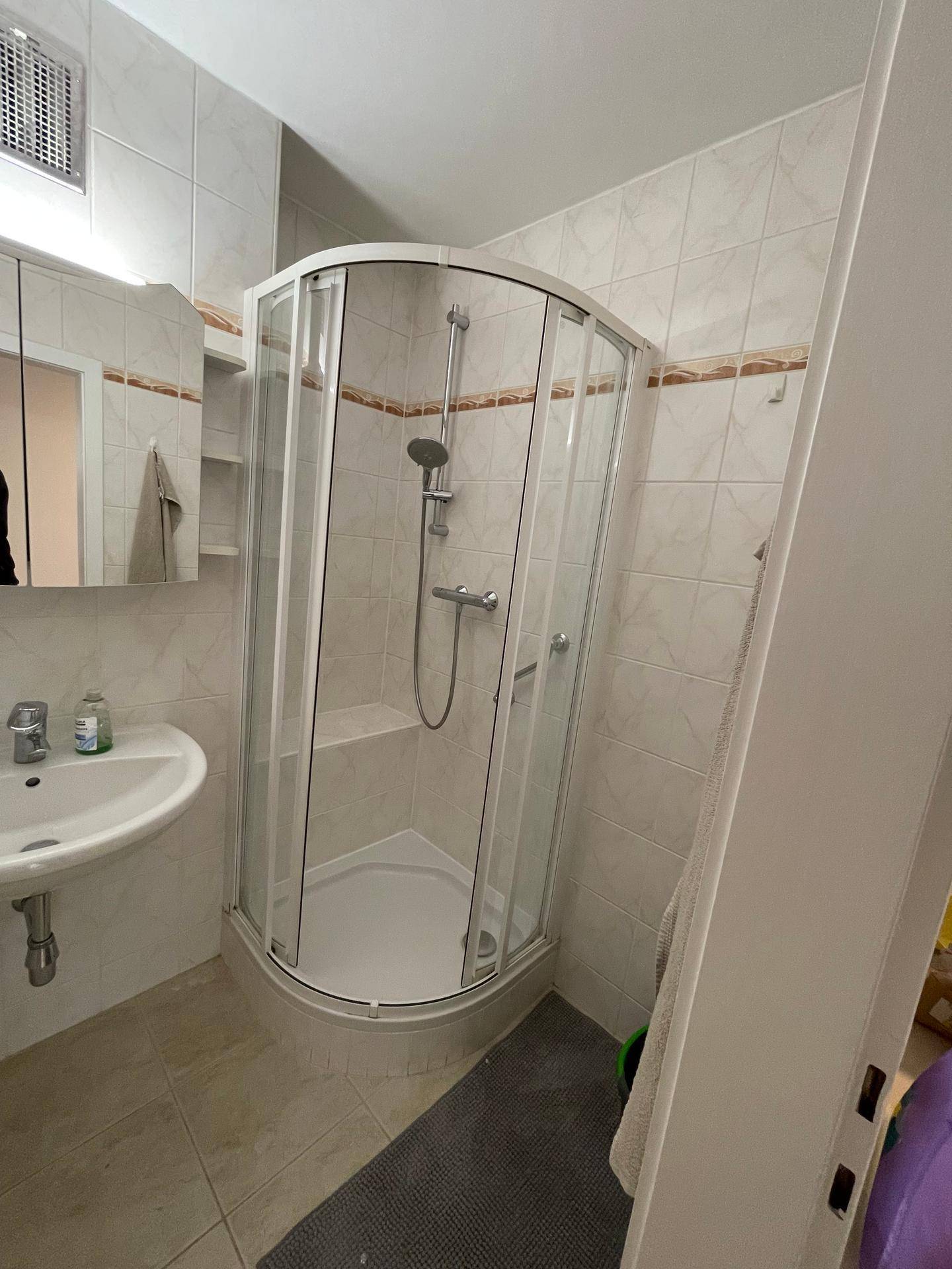 Detaillierte Ansicht der Duschkabine im Badezimmer mit hellen Fliesen und funktionaler Ausstattung.
