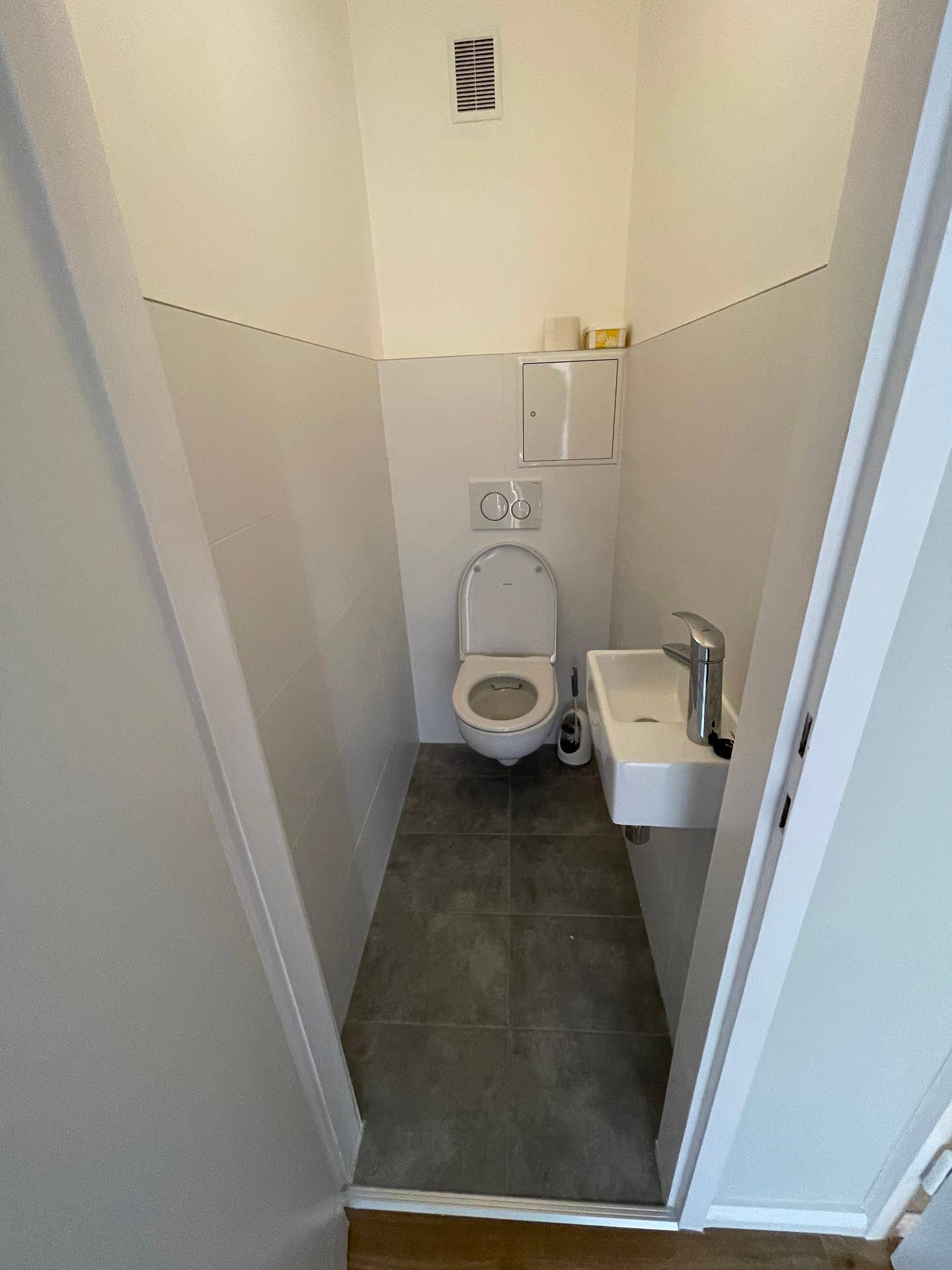 Modernes Gäste-WC mit dunklen Fliesen und weißer Wandverkleidung, ausgestattet mit Toilette und Waschbecken.