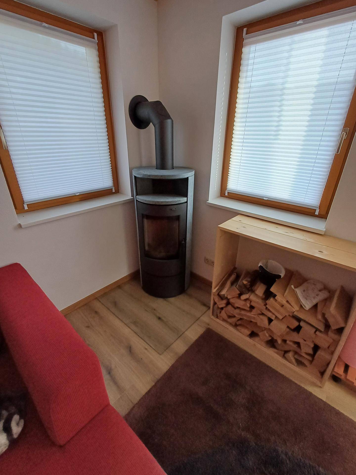 Gemütlicher Wohnbereich mit modernem Holzofen und bereitliegendem Brennholz.