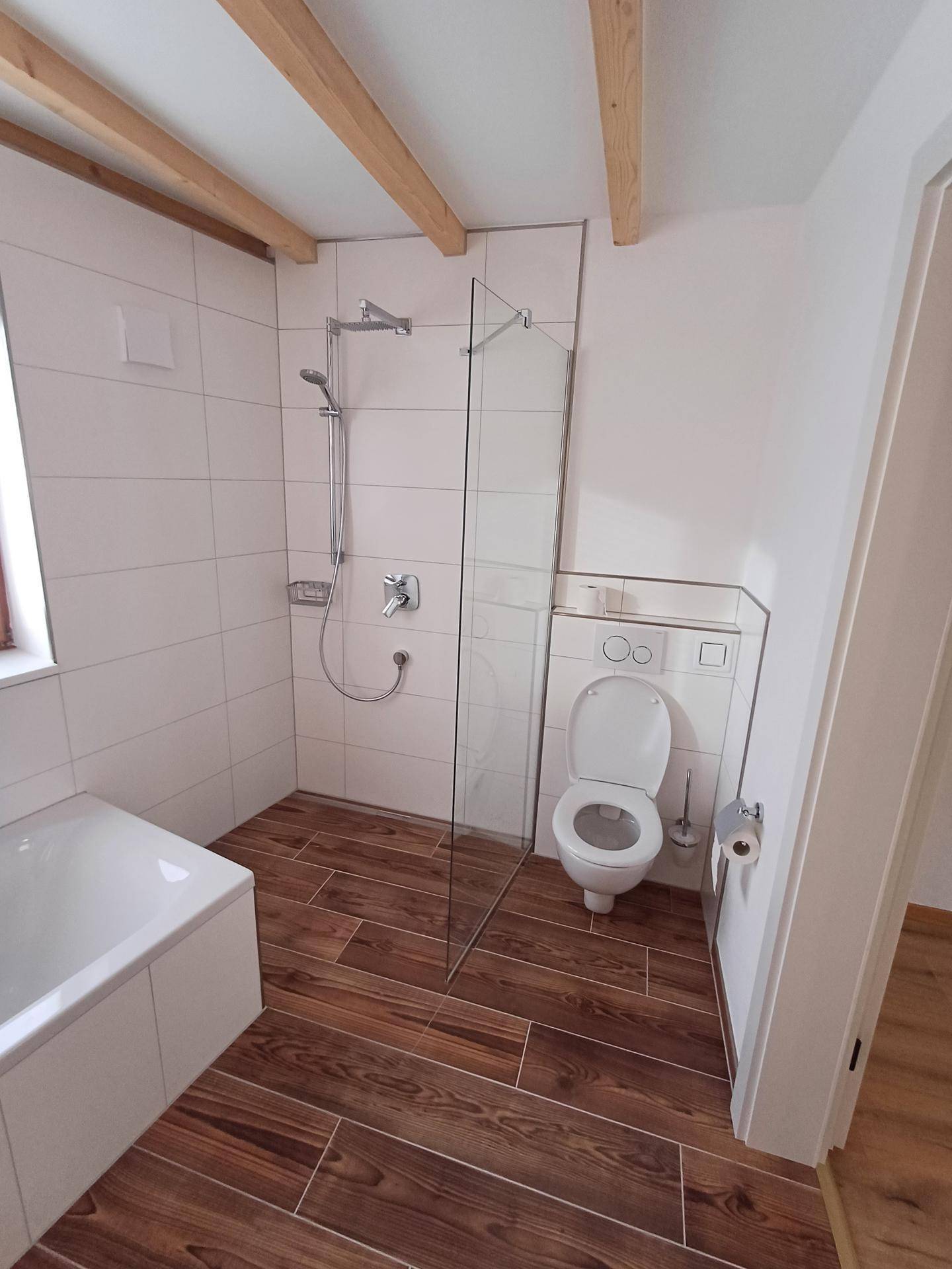 Modernes Badezimmer mit ebenerdiger Dusche, WC und Fliesen in Holzoptik.