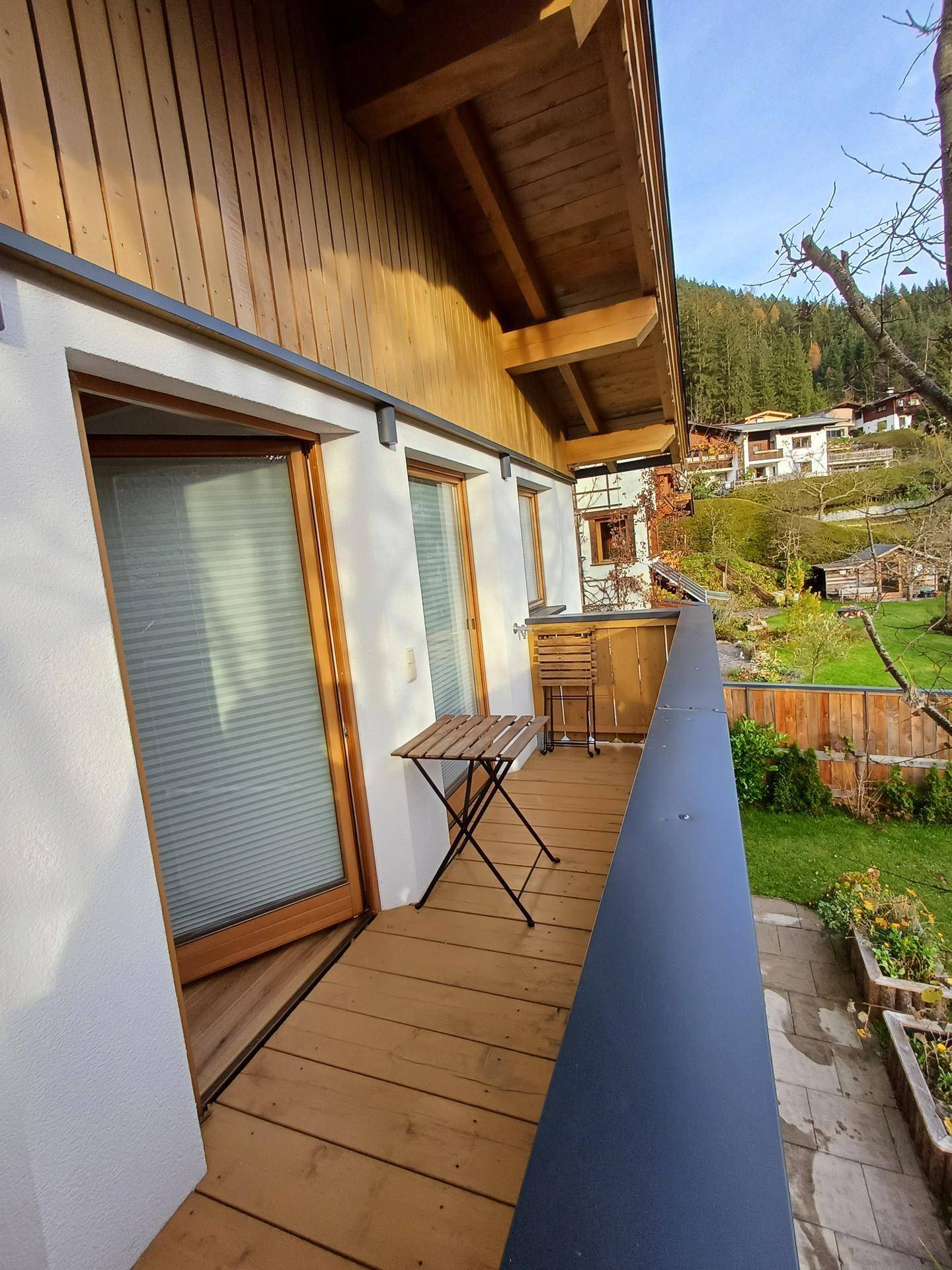 Langer Balkon mit Holzboden und Blick ins Grüne, ausgestattet mit einem kleinen Tisch.