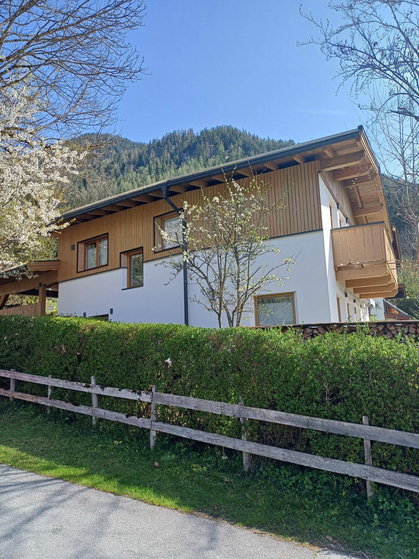 Das Haus im alpinen Stil mit gepflegter Hecke und Bergblick unter blauem Himmel.