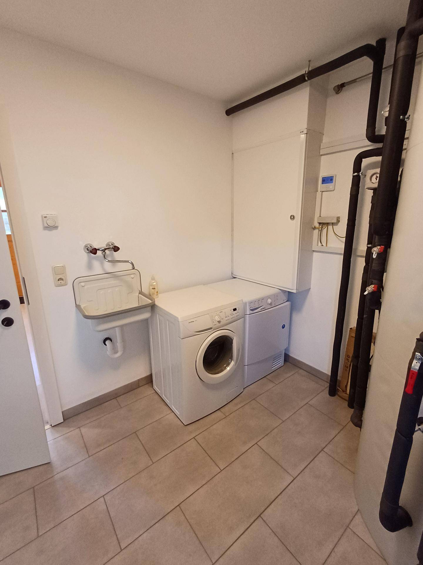 Hauswirtschaftsraum mit Waschmaschine, Trockner und kleinem Waschbecken.