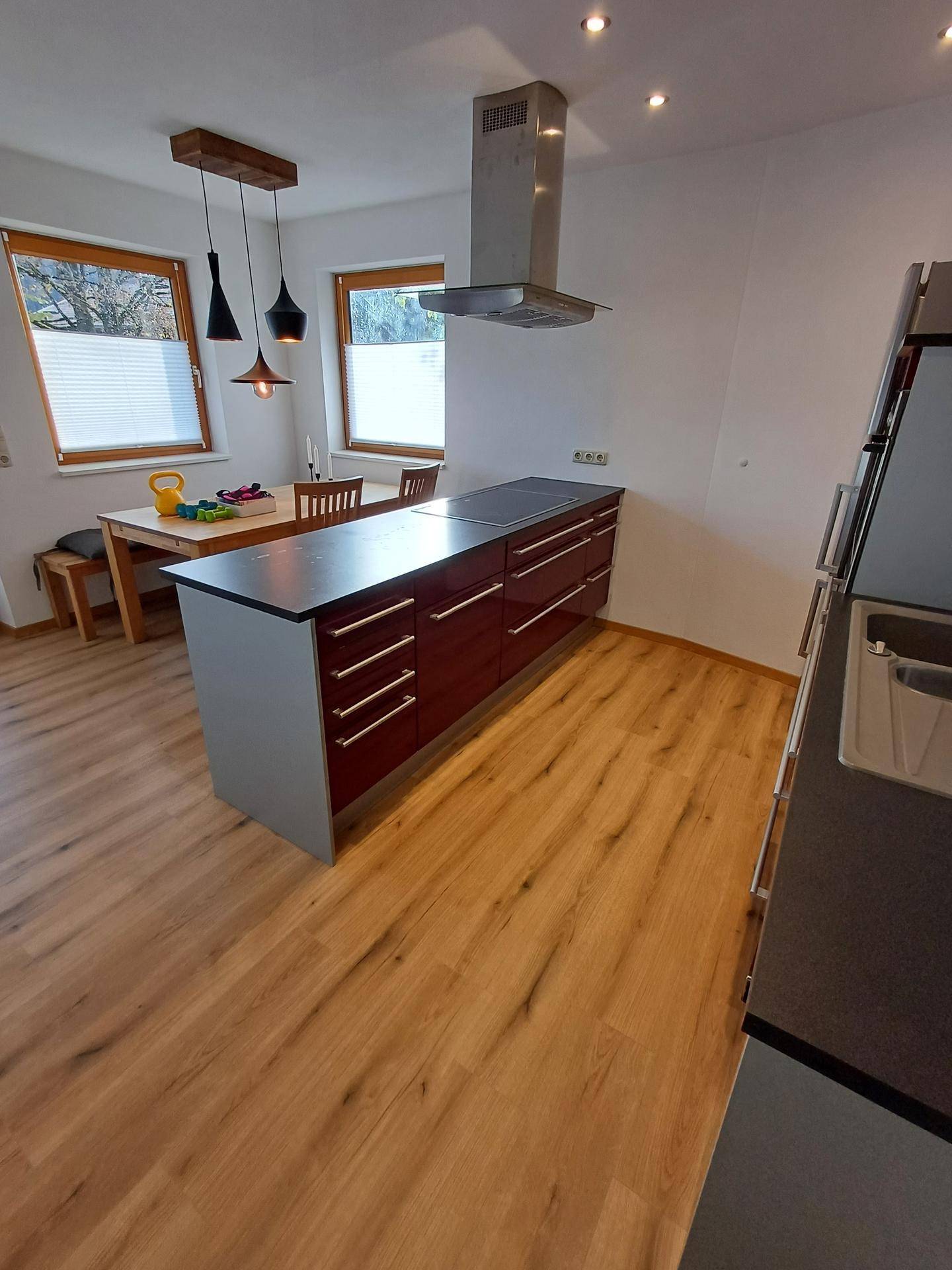 Offene Küche mit Essbereich, Kücheninsel und hellem Laminatboden unter Deckenspots.