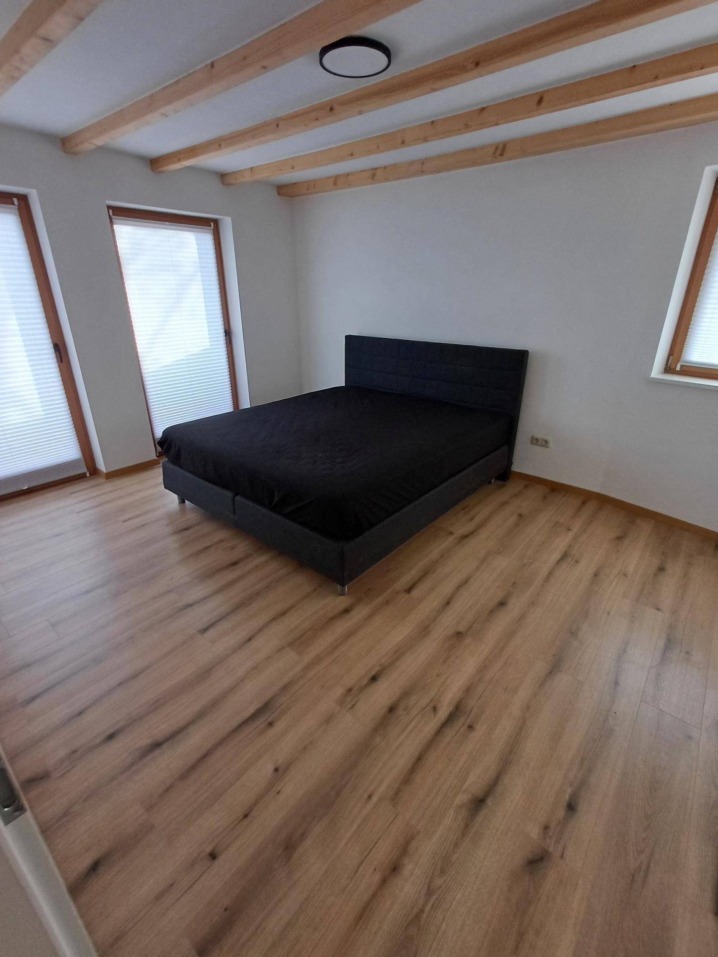 Schlafzimmer mit Doppelbett, sichtbaren Holzbalken an der Decke und Laminatboden.
