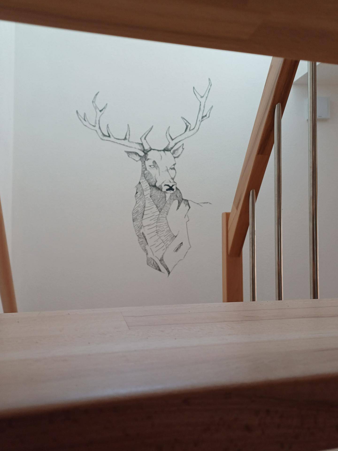 Wanddekoration mit Hirschmotiv neben der Holztreppe, die zum Obergeschoss führt.