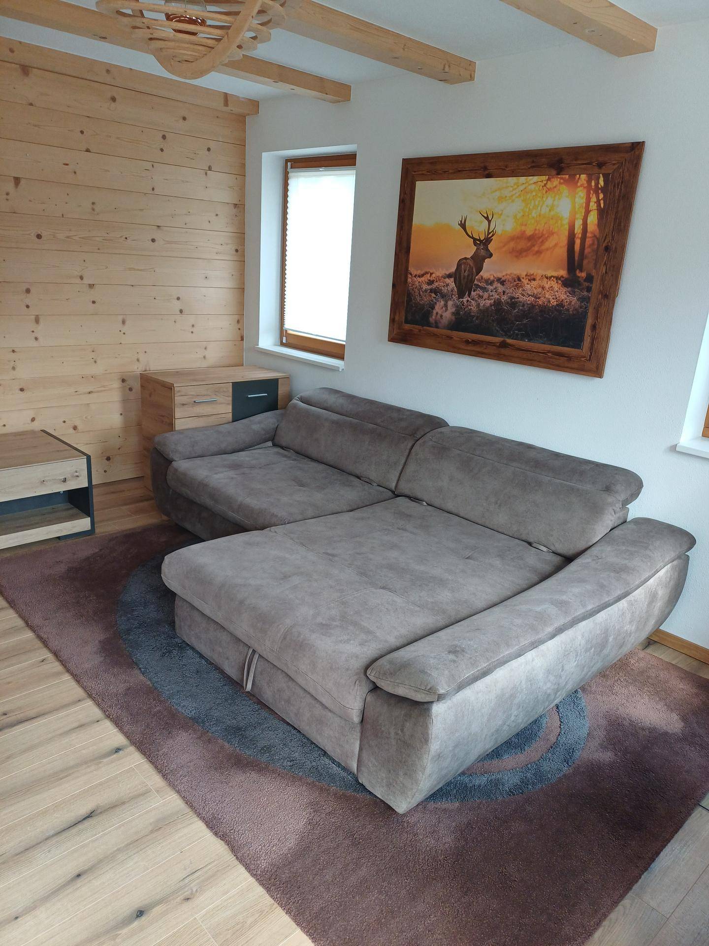 Gemütliches Wohnzimmer mit großem Sofa, Holzwandverkleidung und rustikalem Hirschbild.