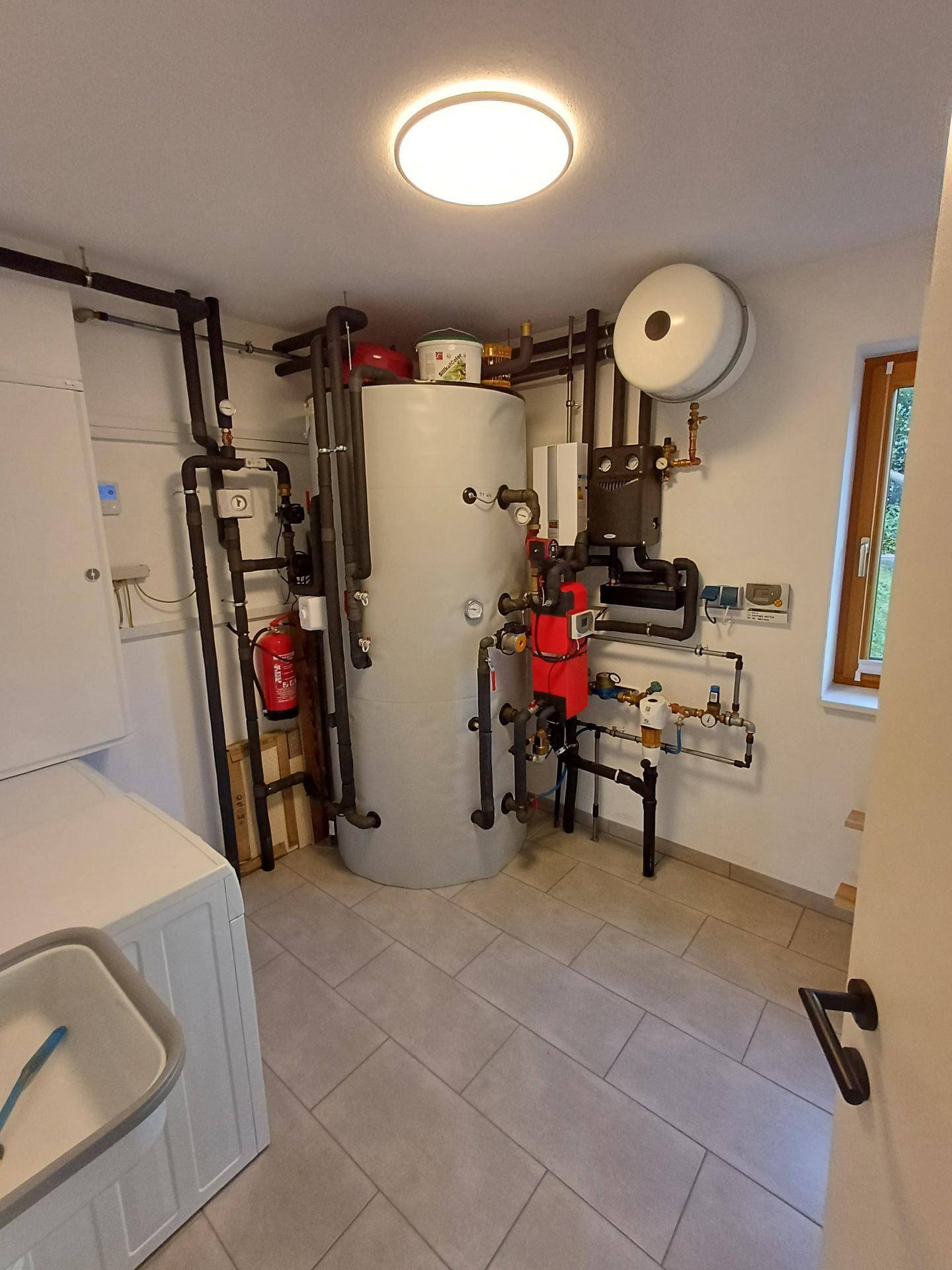 Heizungsraum mit Warmwasserspeicher und komplexer Rohrinstallation.