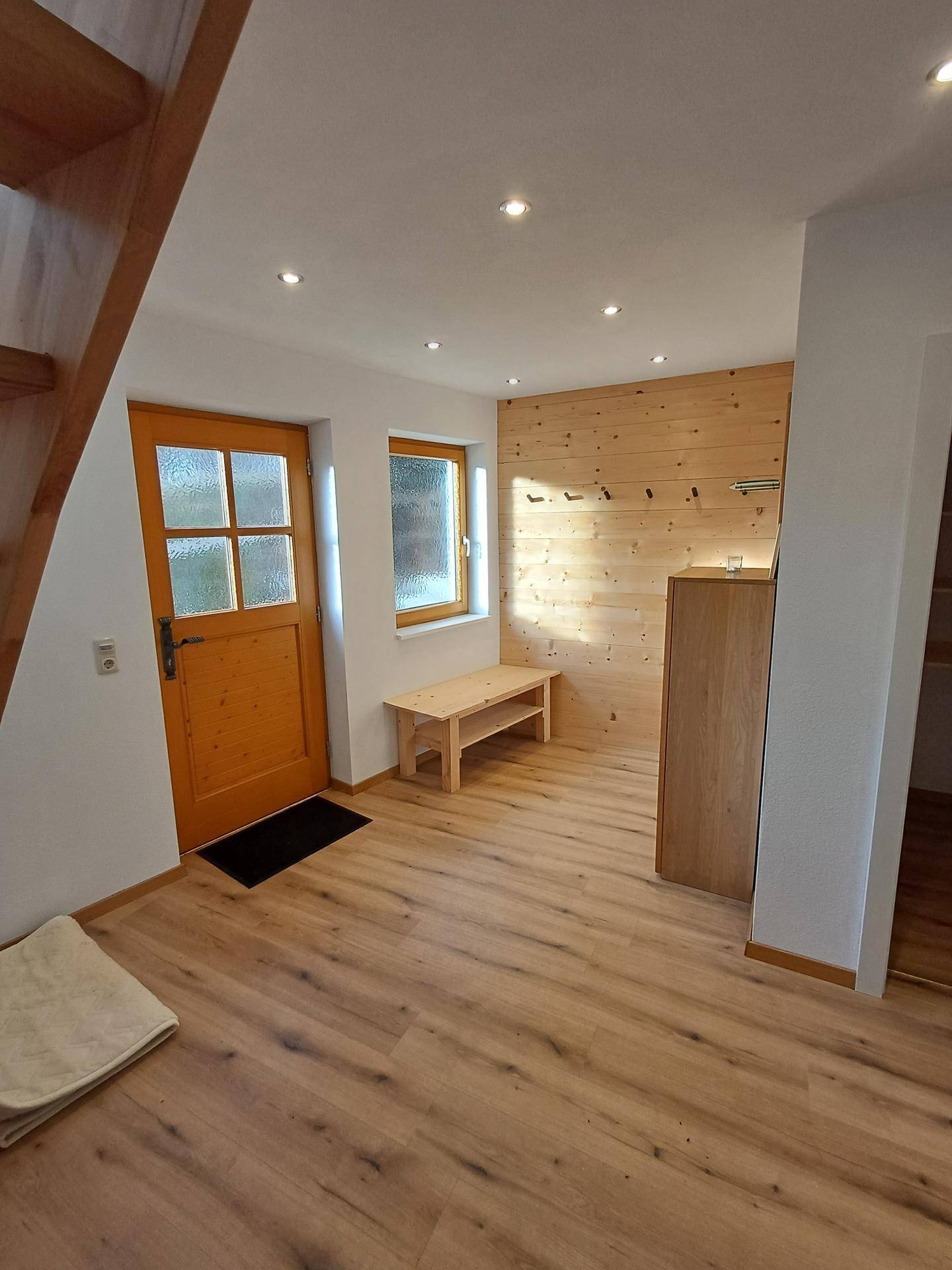 Heller Eingangsbereich mit Holzboden, Holzvertäfelung und einer Holztreppe, die nach oben führt.