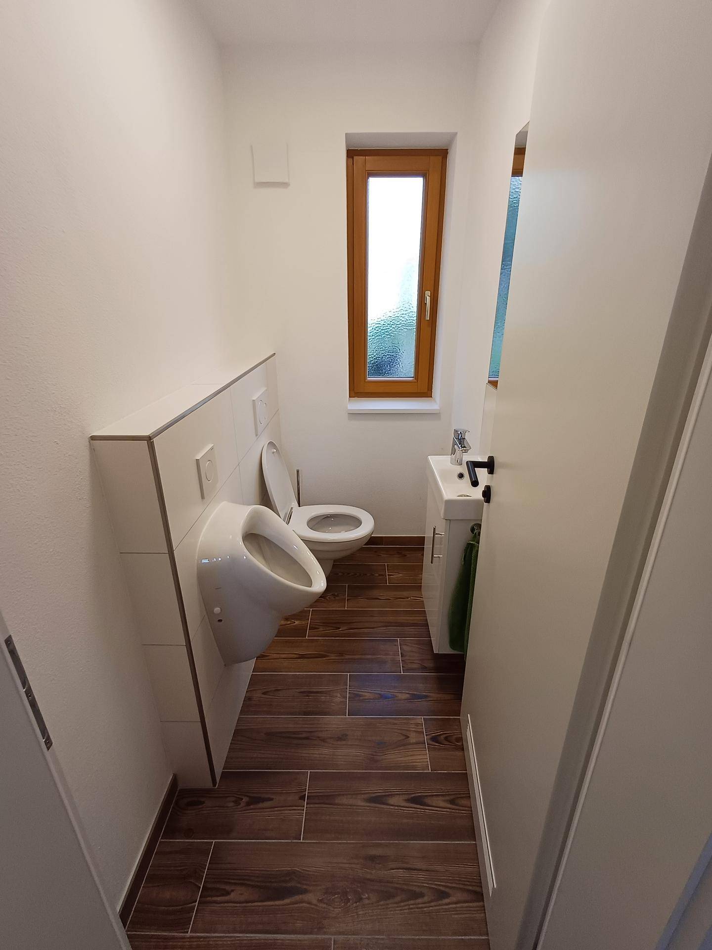 Gäste-WC mit Urinal, Toilette und kleinem Waschbecken, ausgestattet mit Fenster.
