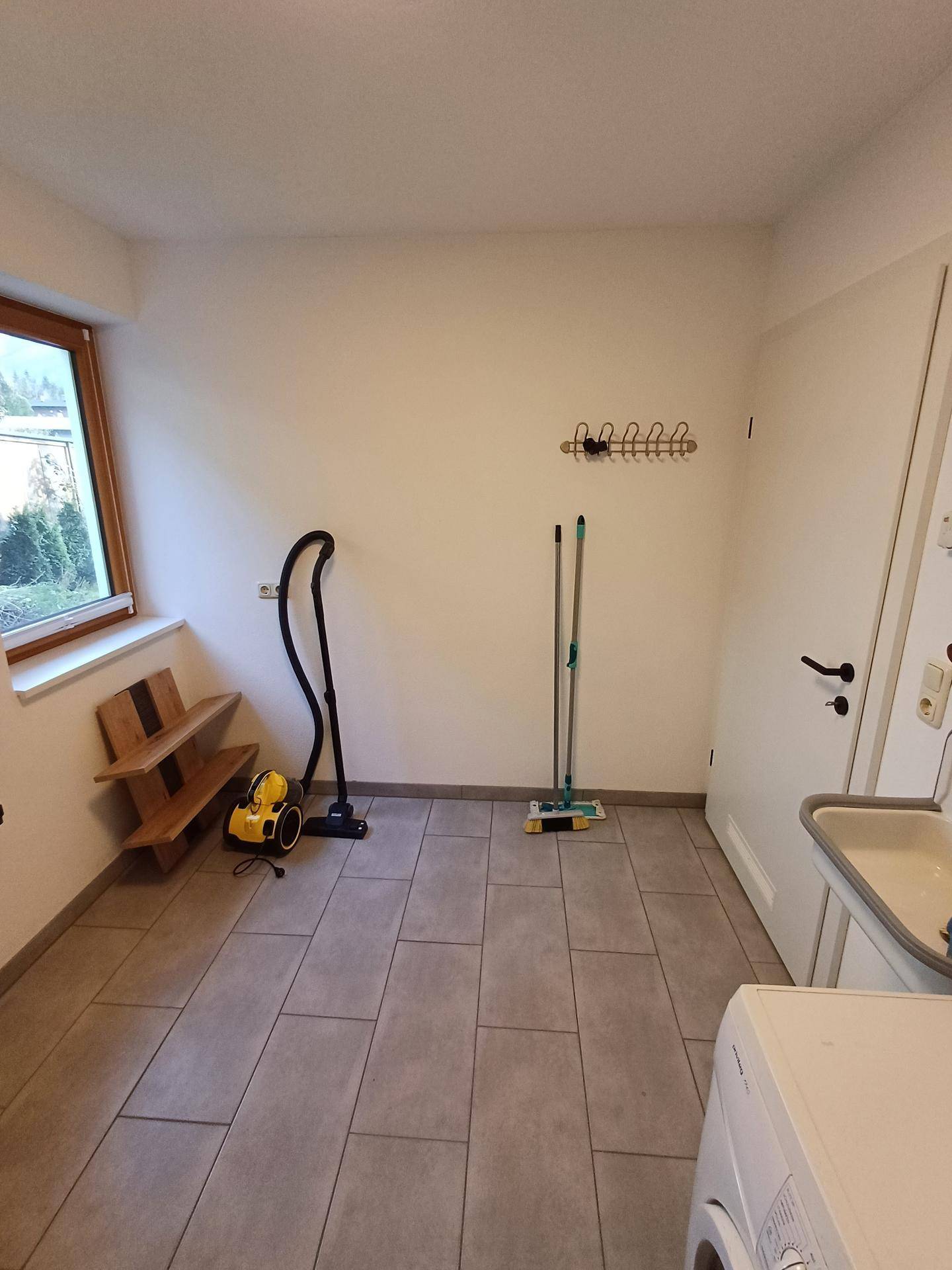 Hauswirtschaftsraum mit Waschmaschine, Spülbecken und Stauraum für Reinigungsgeräte.