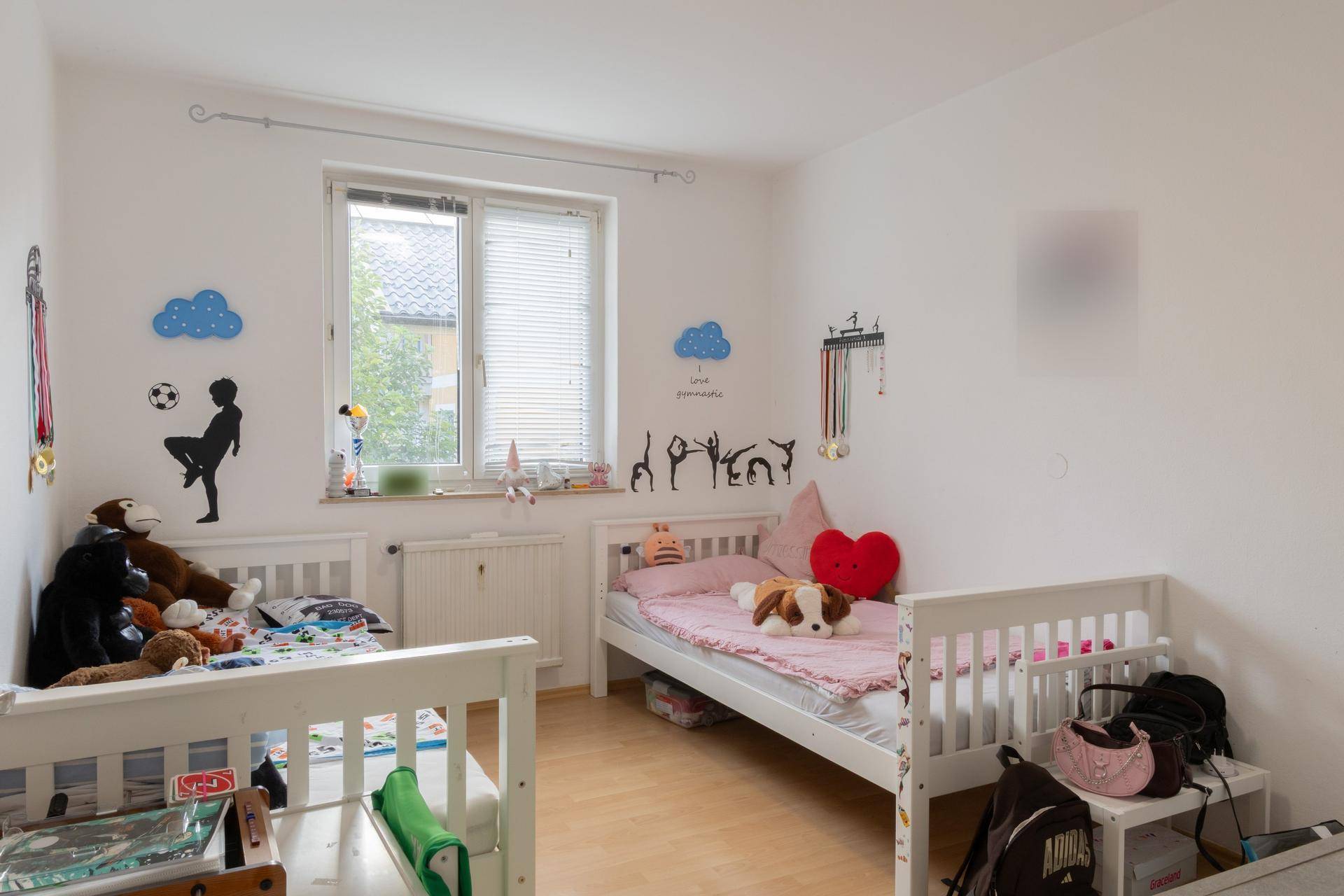 Kinderzimmer mit zwei Einzelbetten, hellem Laminatboden und spielerischer Wanddekoration.