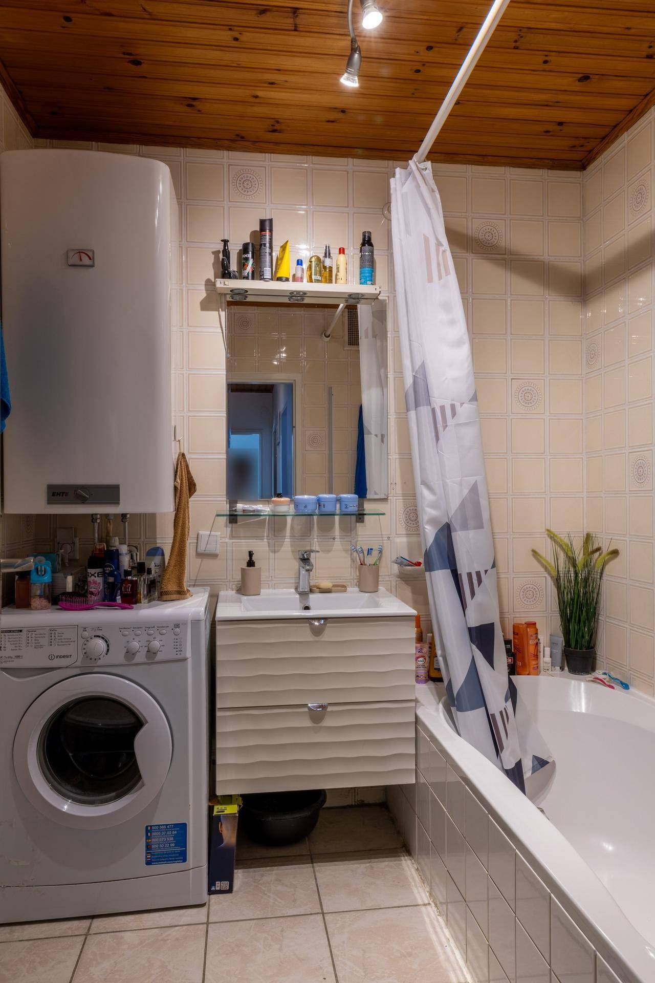 Badezimmer mit Badewanne, Waschmaschine, Waschbecken und gefliesten Wänden.