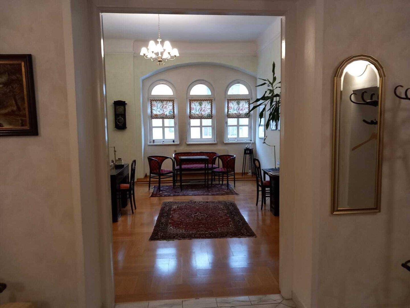 Blick vom Flur in ein klassisches Büro mit Holzboden, antiken Möbeln und großen Bogenfenstern.