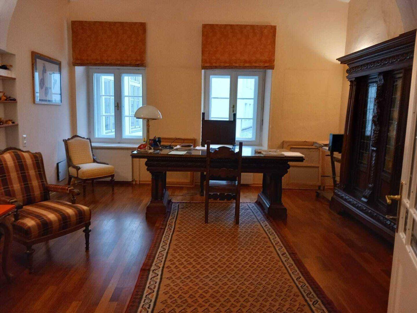 Geräumiges Büro mit dunklem Holzboden, großem Schreibtisch und einem antiken Holzschrank.