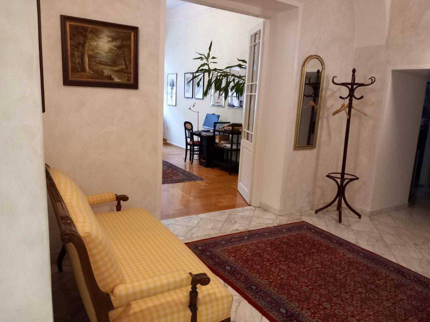 Heller Flur mit Fliesenboden und einem Blick in ein angrenzendes Zimmer mit Holzboden.