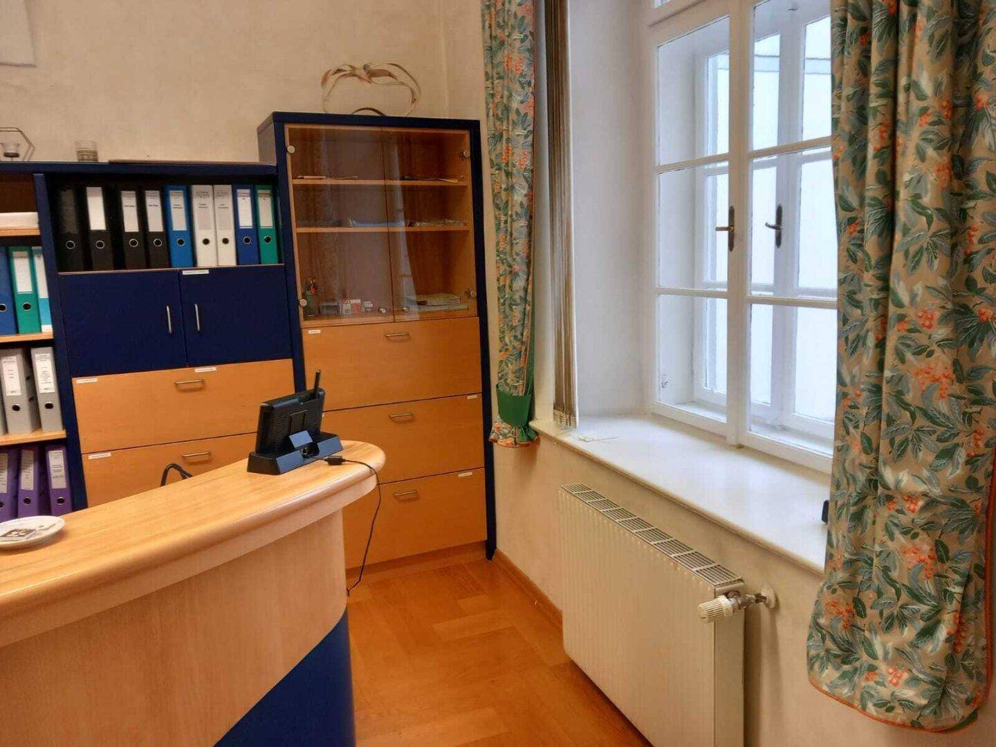 Fensterbereich in einem Büro mit Heizkörper, Vorhängen und Blick nach draußen.