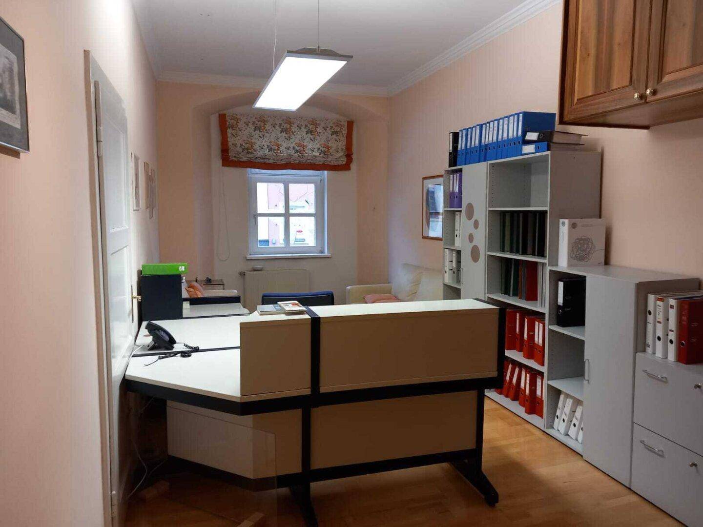 Helles Büro mit Holzboden, modernem Schreibtisch und Regalen voller Aktenordner.
