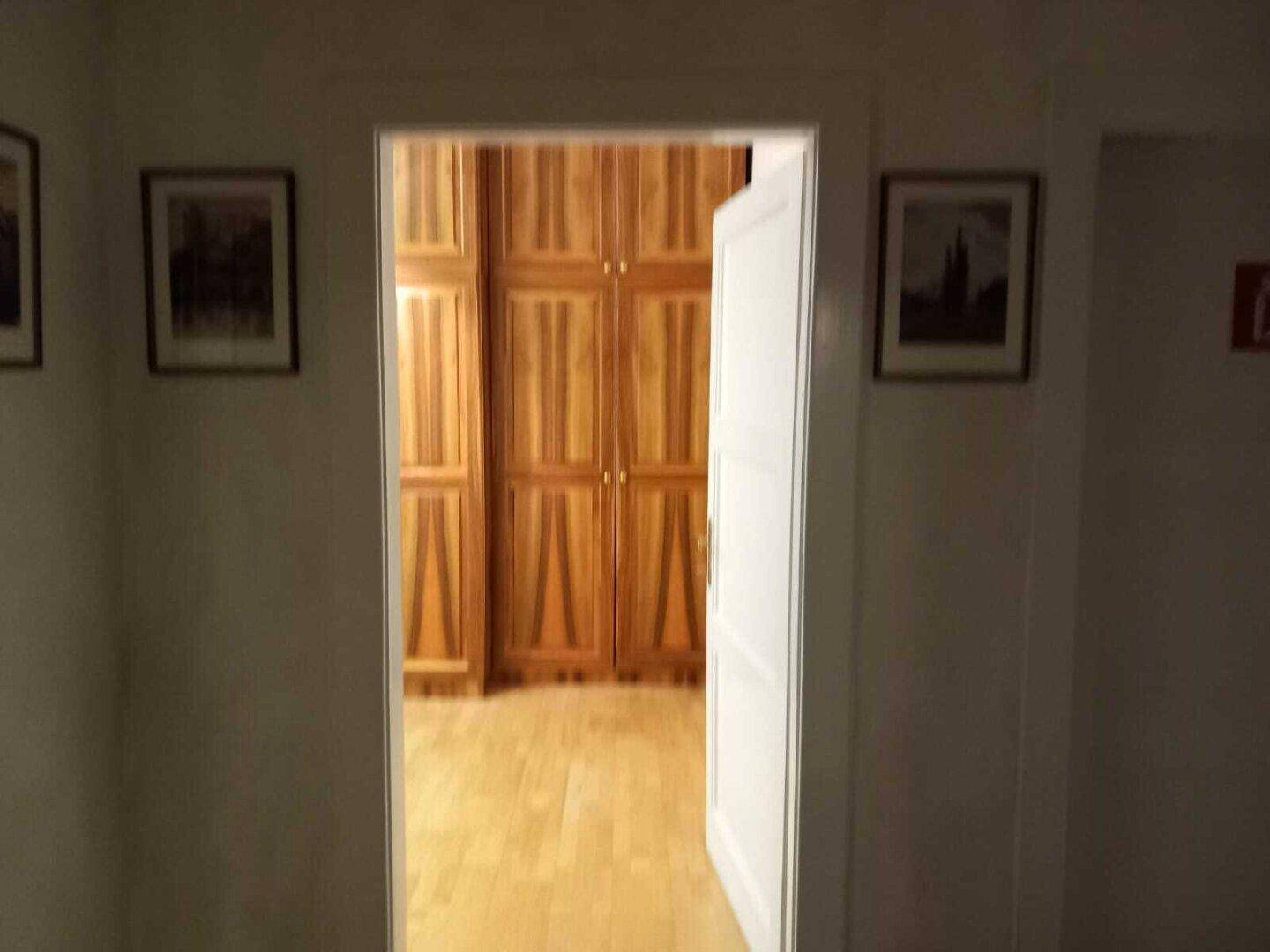 Offene Tür zu einem Raum mit Holzboden und hohen Holzschränken.