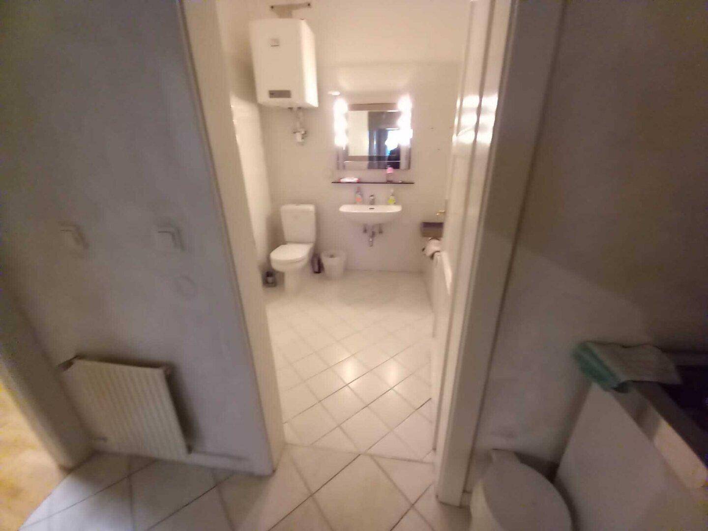 Blick vom Flur in ein helles Badezimmer mit weißen Fliesen und modernen Armaturen.