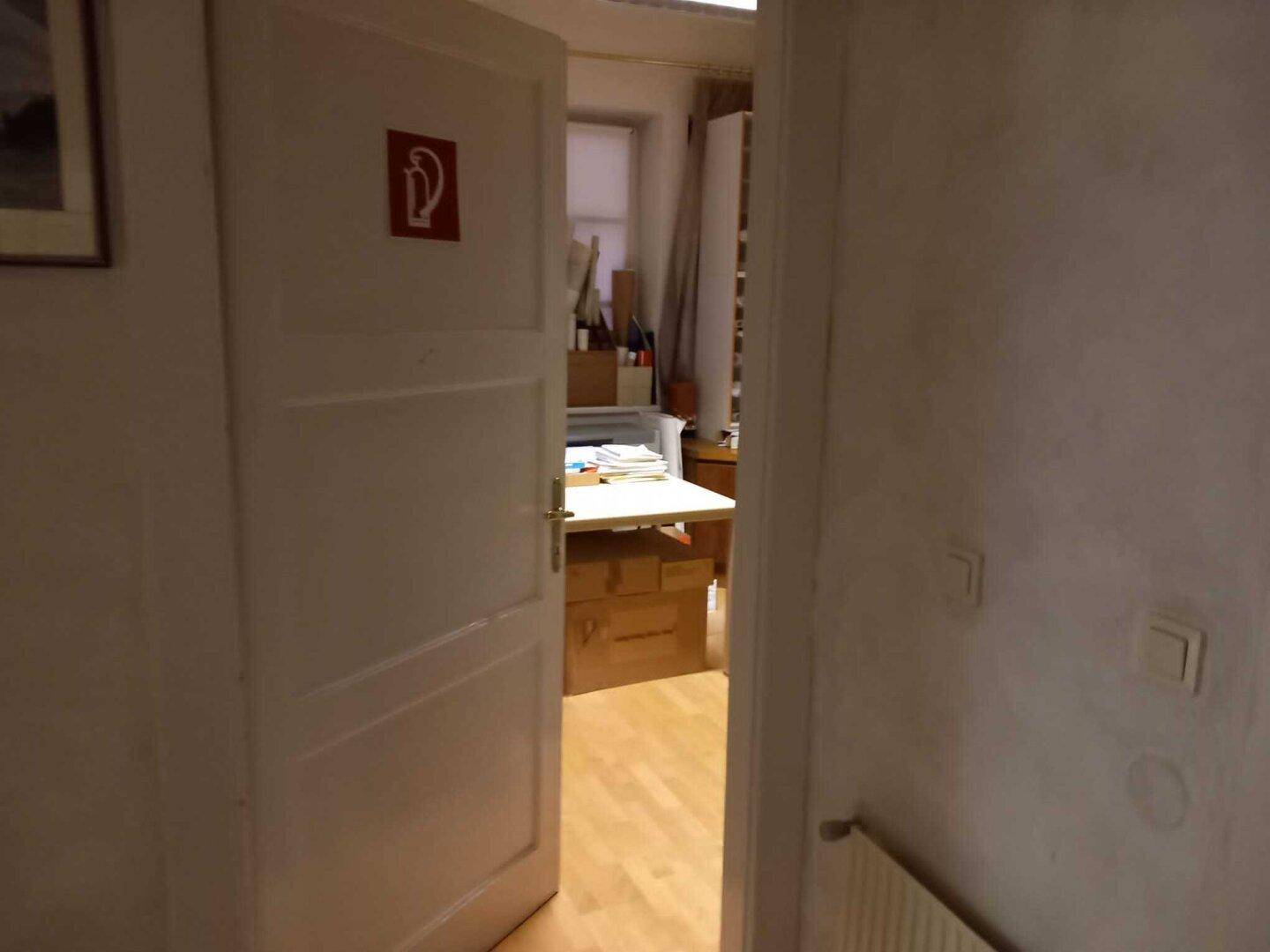 Offene Tür zu einem Abstellraum mit Holzboden und Regalen voller Dokumente.