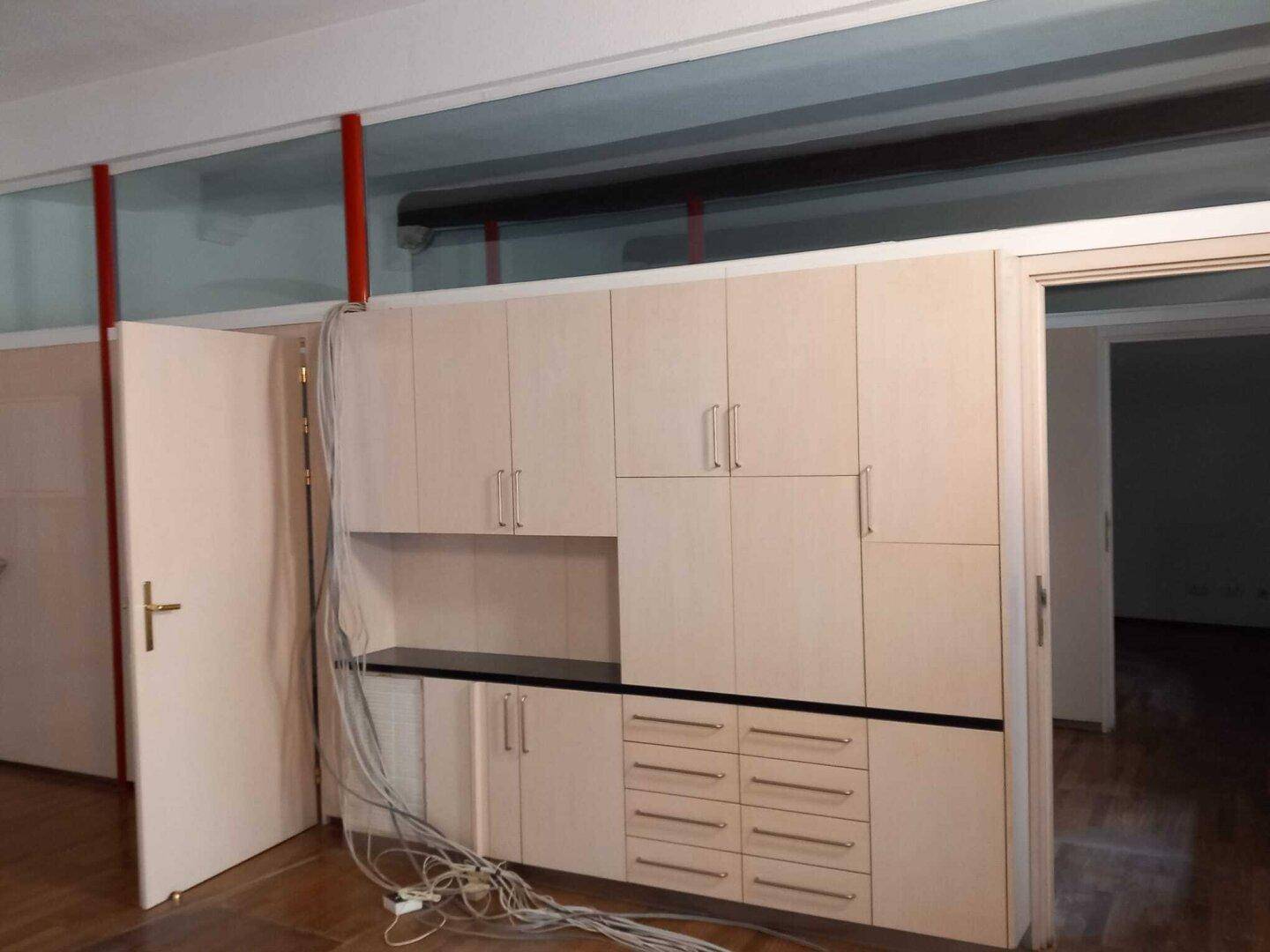 Ein Innenraum mit hellen Einbauschränken, sichtbaren Holzbalken und freiliegenden Kabeln, bereit zur Einrichtung.