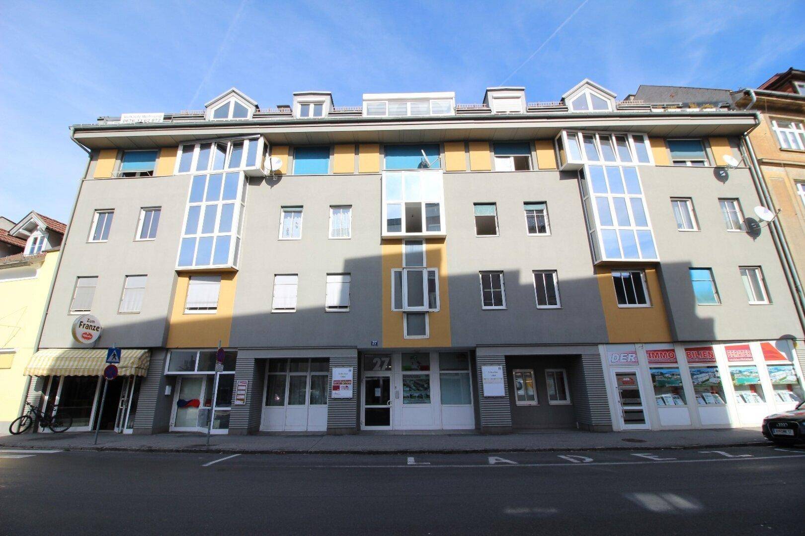Mehrfamilienhaus mit moderner Fassade, großen Fenstern und Dachgauben.