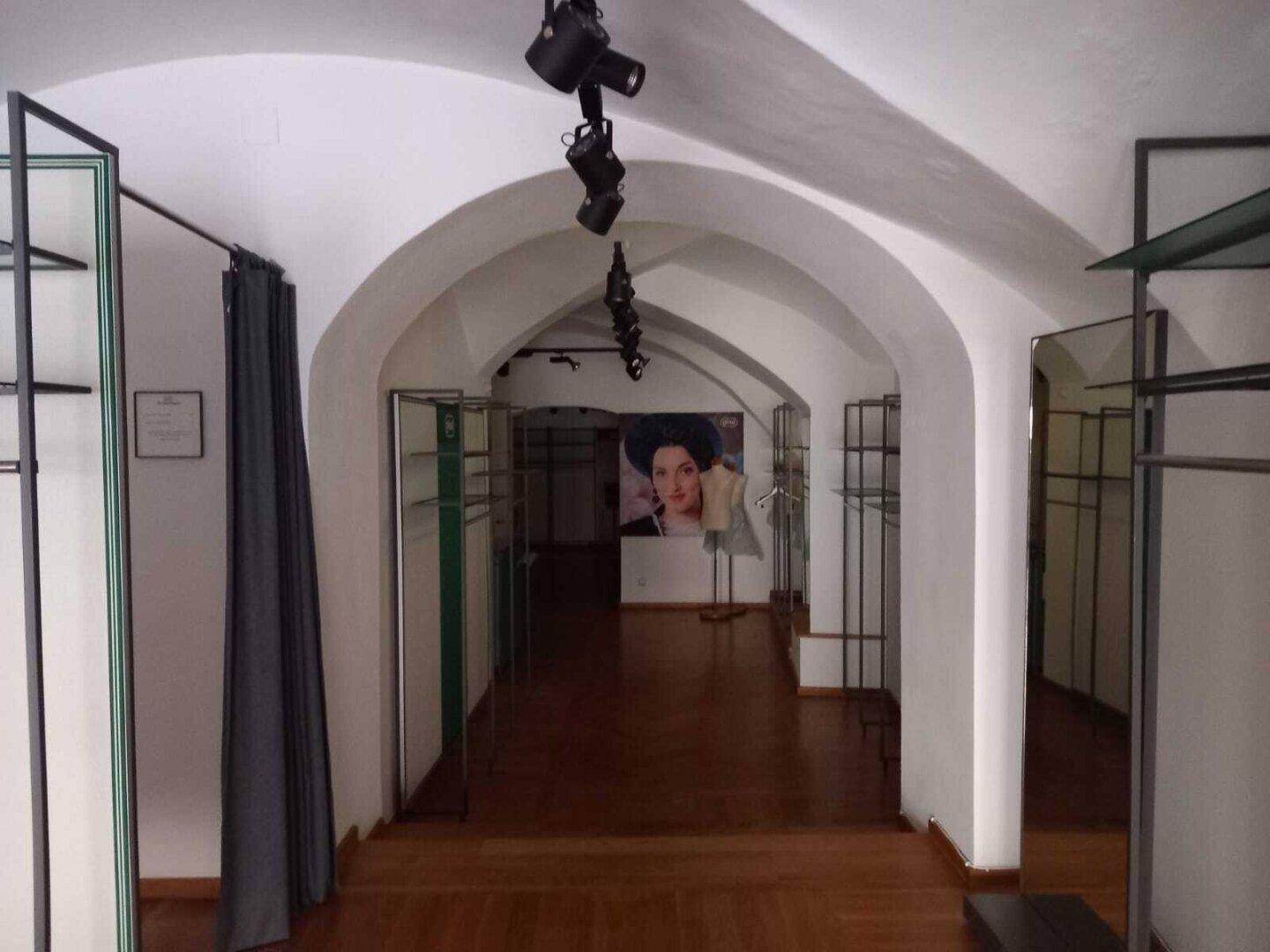 Innenansicht eines Geschäftsraums mit Gewölbedecken, Holzboden und Schaufensterpuppen im Hintergrund, gut beleuchtet.