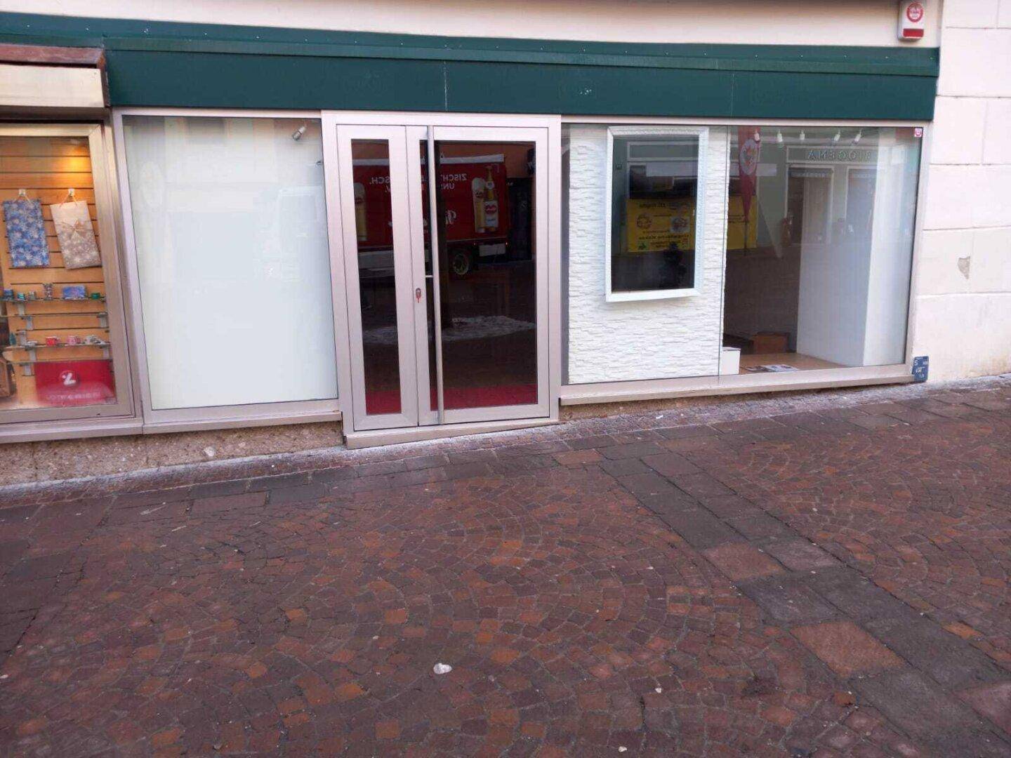 Außenansicht eines Geschäftsgebäudes mit großen Schaufenstern und Eingangstür direkt an der gepflasterten Straße.