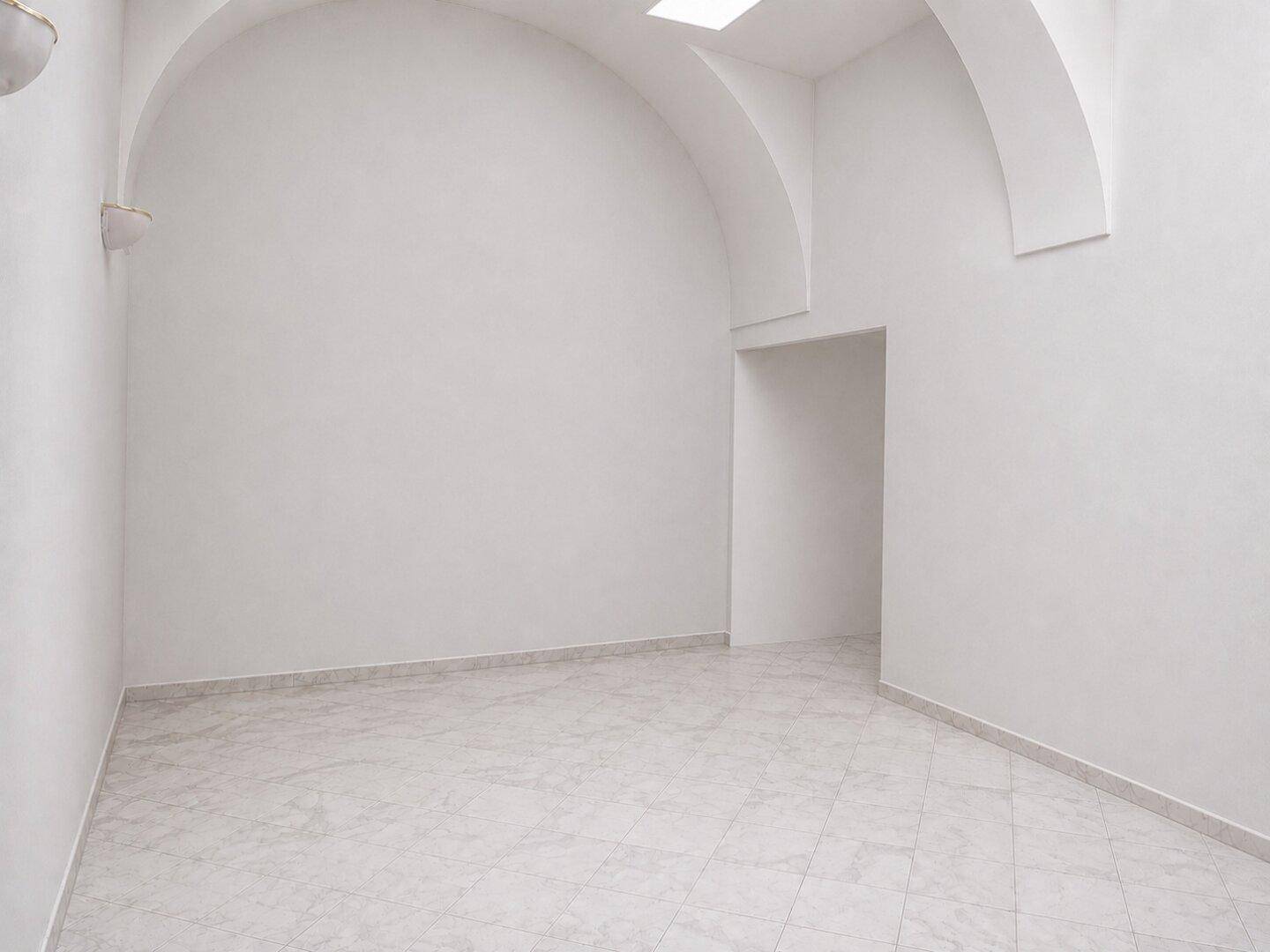 Heller Raum mit weißem Fliesenboden, gewölbter Decke und einem Oberlicht für natürliches Licht.