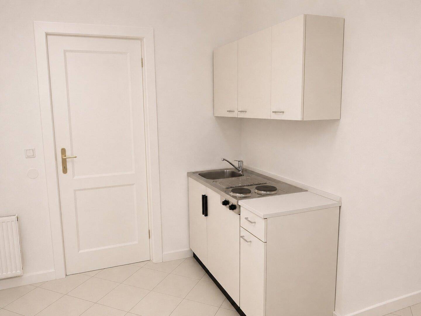 Kompakte Küchenzeile mit weißen Schränken, Spüle und Kochplatten, ideal für kleine Wohnungen.