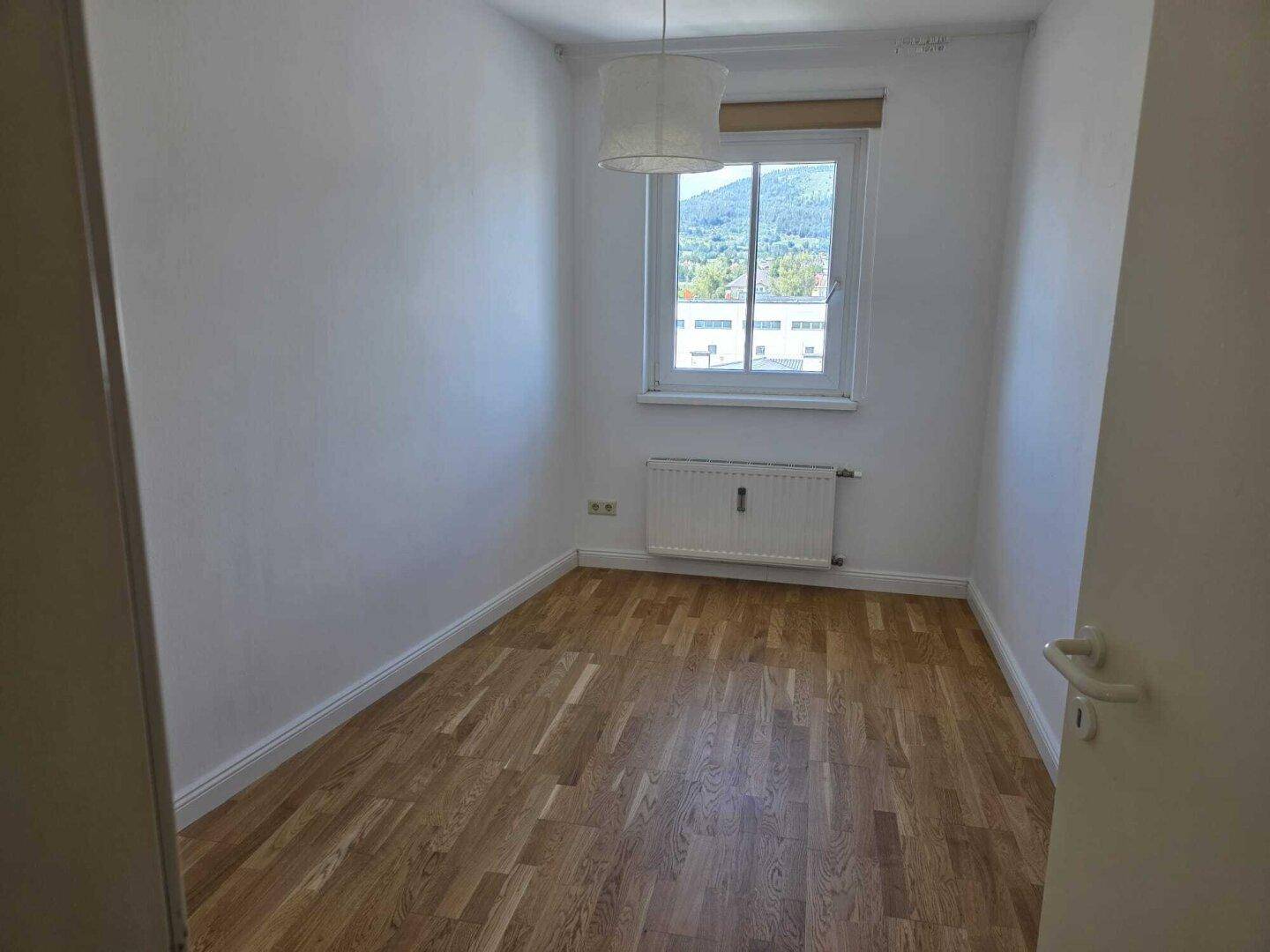 Kleines, helles Zimmer mit Holzboden und Fenster, ideal als Kinder- oder Arbeitszimmer.
