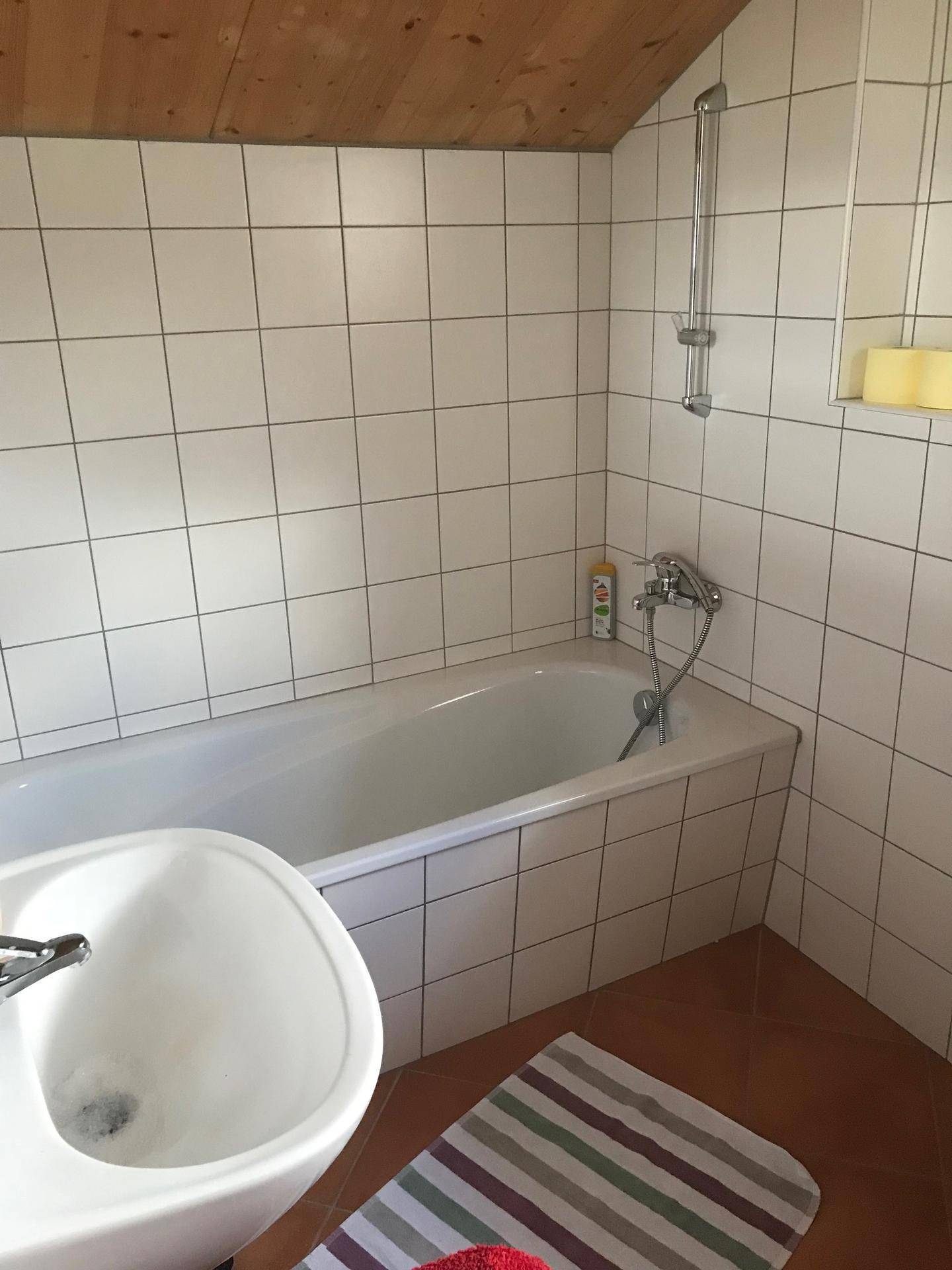 Badezimmer mit Badewanne, Waschbecken und weißen Fliesen in schlichtem Design.