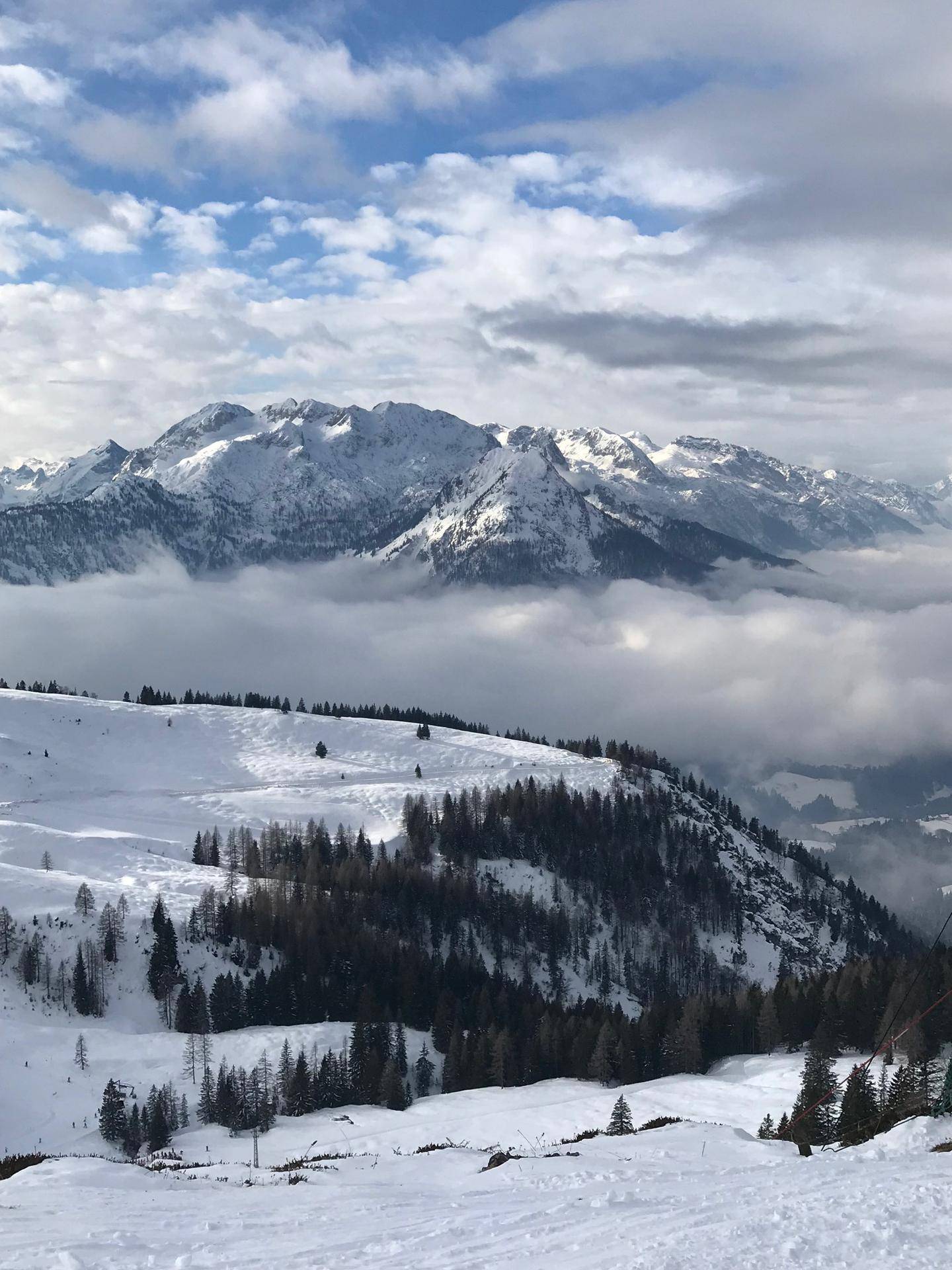 Panoramablick auf schneebedeckte Berge und Wolkenformationen über den Tälern.
