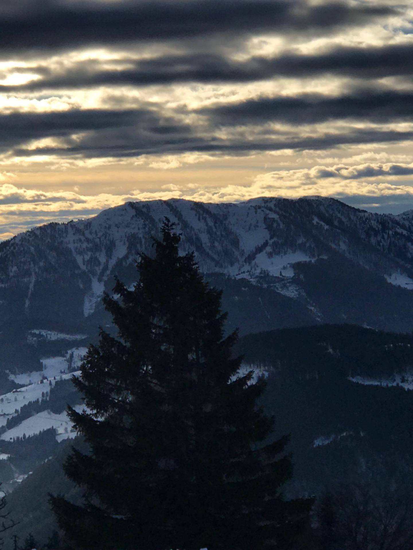Dramatischer Sonnenuntergang über schneebedeckten Bergen und Tälern mit dunklen Wolken.