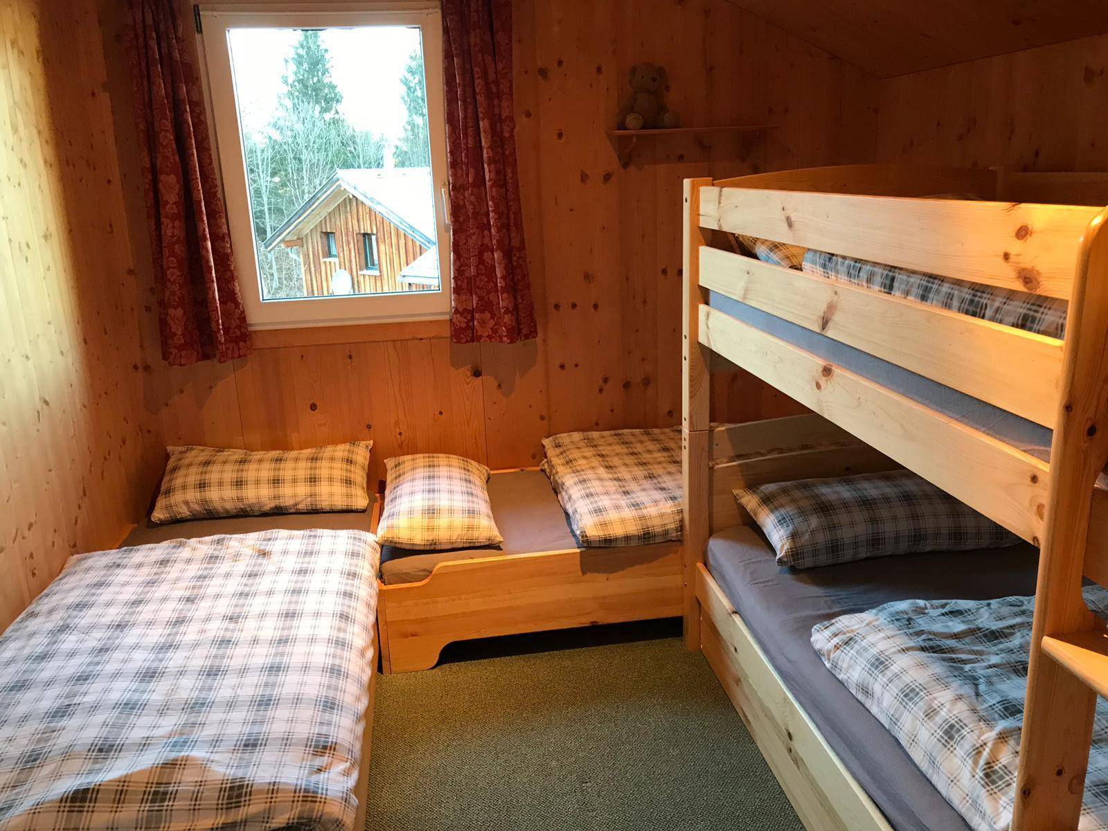 Kinderzimmer mit Etagenbett, Einzelbetten und Blick auf die verschneite Landschaft.