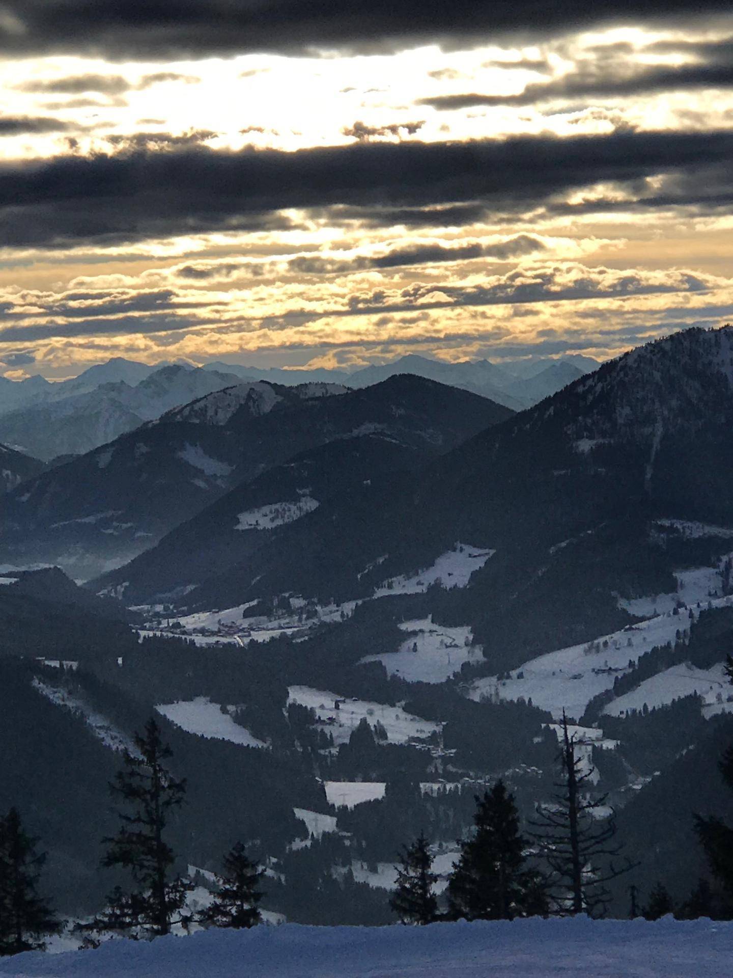 Weitläufiger Blick über schneebedeckte Täler und Berge unter einem dramatischen Himmel.
