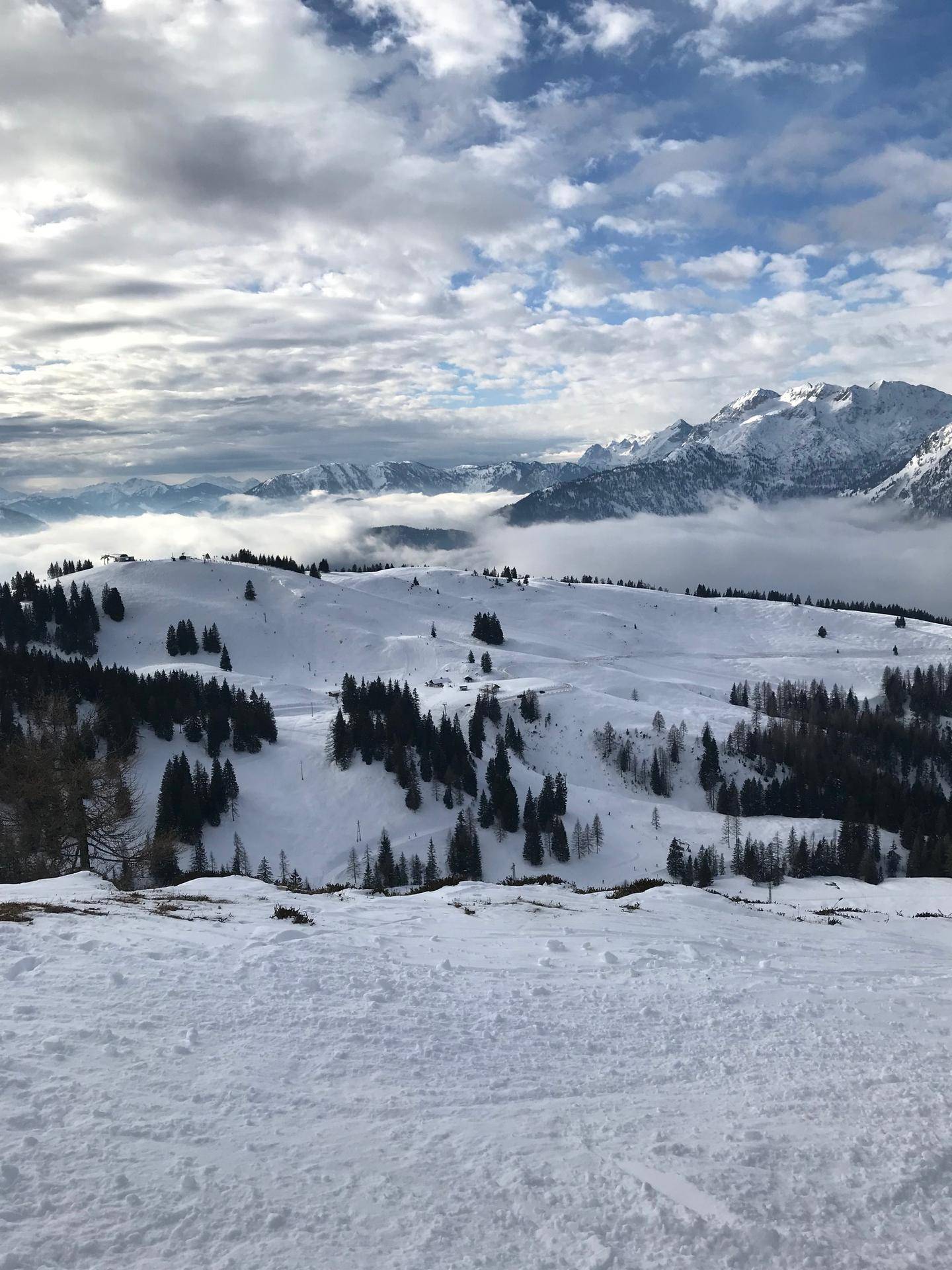 Panoramablick auf ein Skigebiet mit schneebedeckten Hügeln und Wäldern über den Wolken.