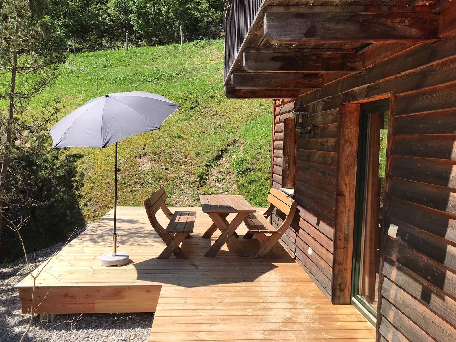 Gemütliche Holzterrasse mit Sitzgelegenheiten und Sonnenschirm, umgeben von Natur.