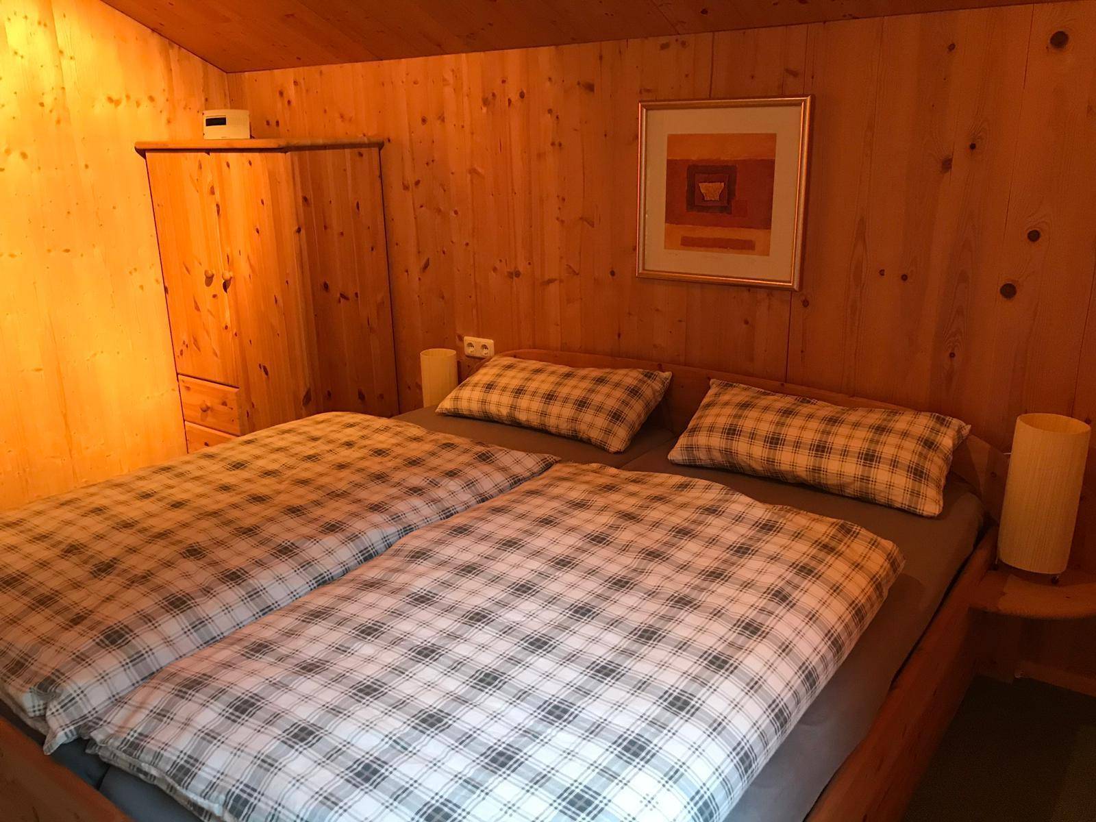 Schlafzimmer mit Holzvertäfelung, Doppelbett und einem Kleiderschrank aus hellem Holz.