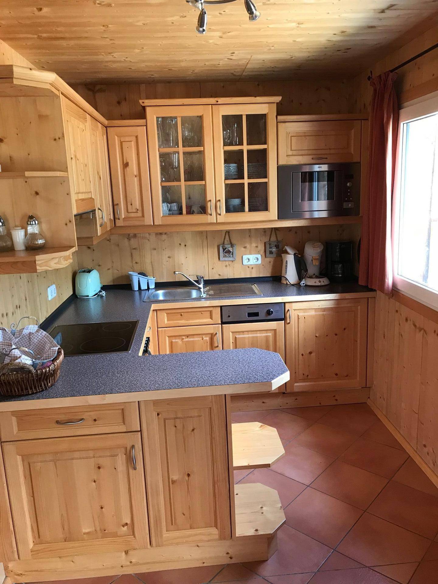 Rustikale Holzküche mit Einbaugeräten, dunkler Arbeitsplatte und Terracotta-Fliesenboden.