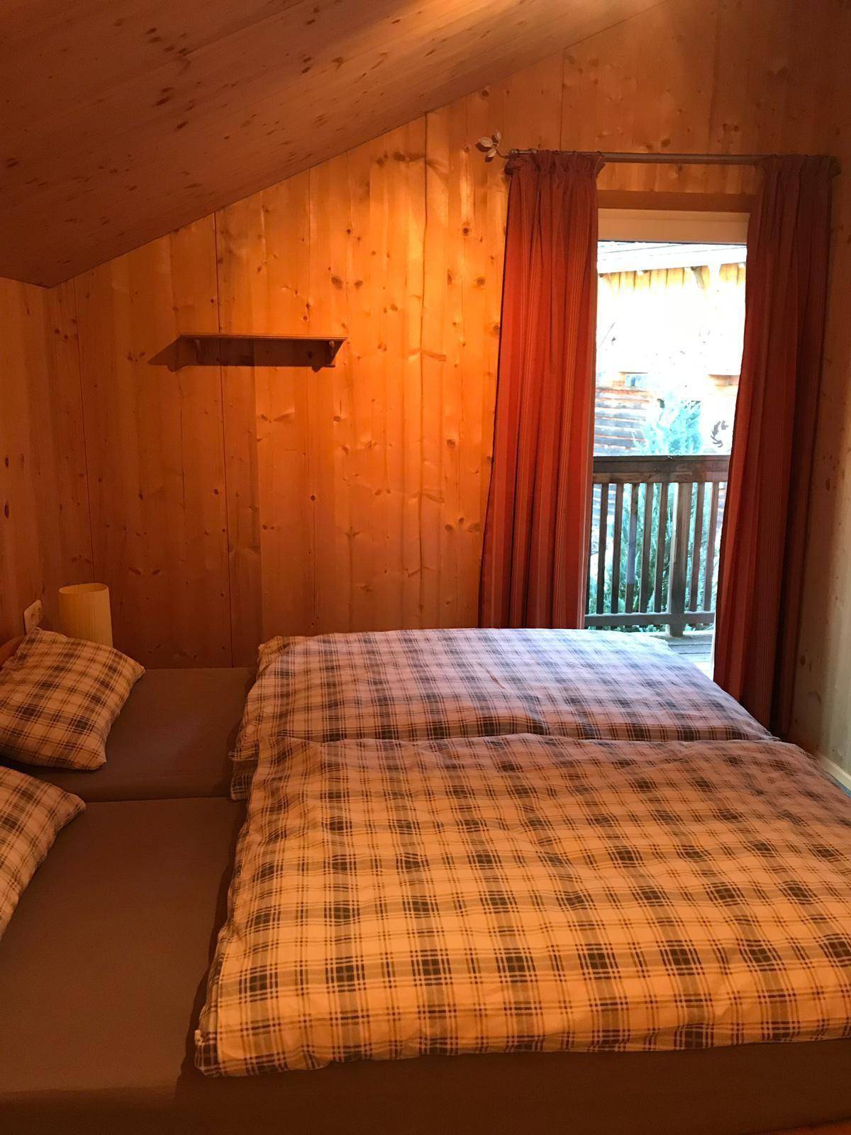 Schlafzimmer mit Holzvertäfelung, Doppelbett und Zugang zu einem kleinen Balkon.