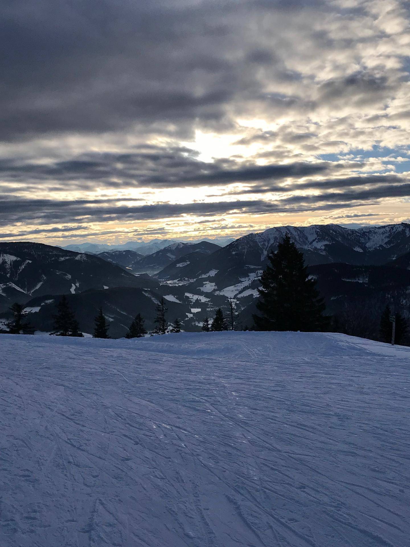 Panoramablick auf schneebedeckte Berge und Täler mit einem beeindruckenden Wolkenhimmel.